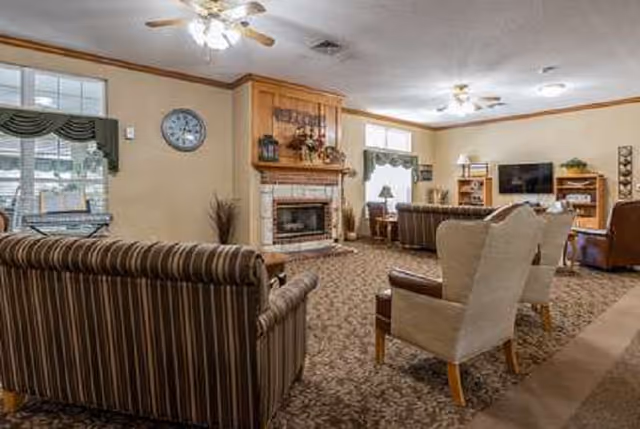 Cozy senior living lounge with striped sofas, armchairs, a fireplace, and a mounted TV.