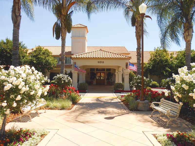 Entrance to Oakmont of Escondido Hills with palm trees, benches, and a covered walkway.