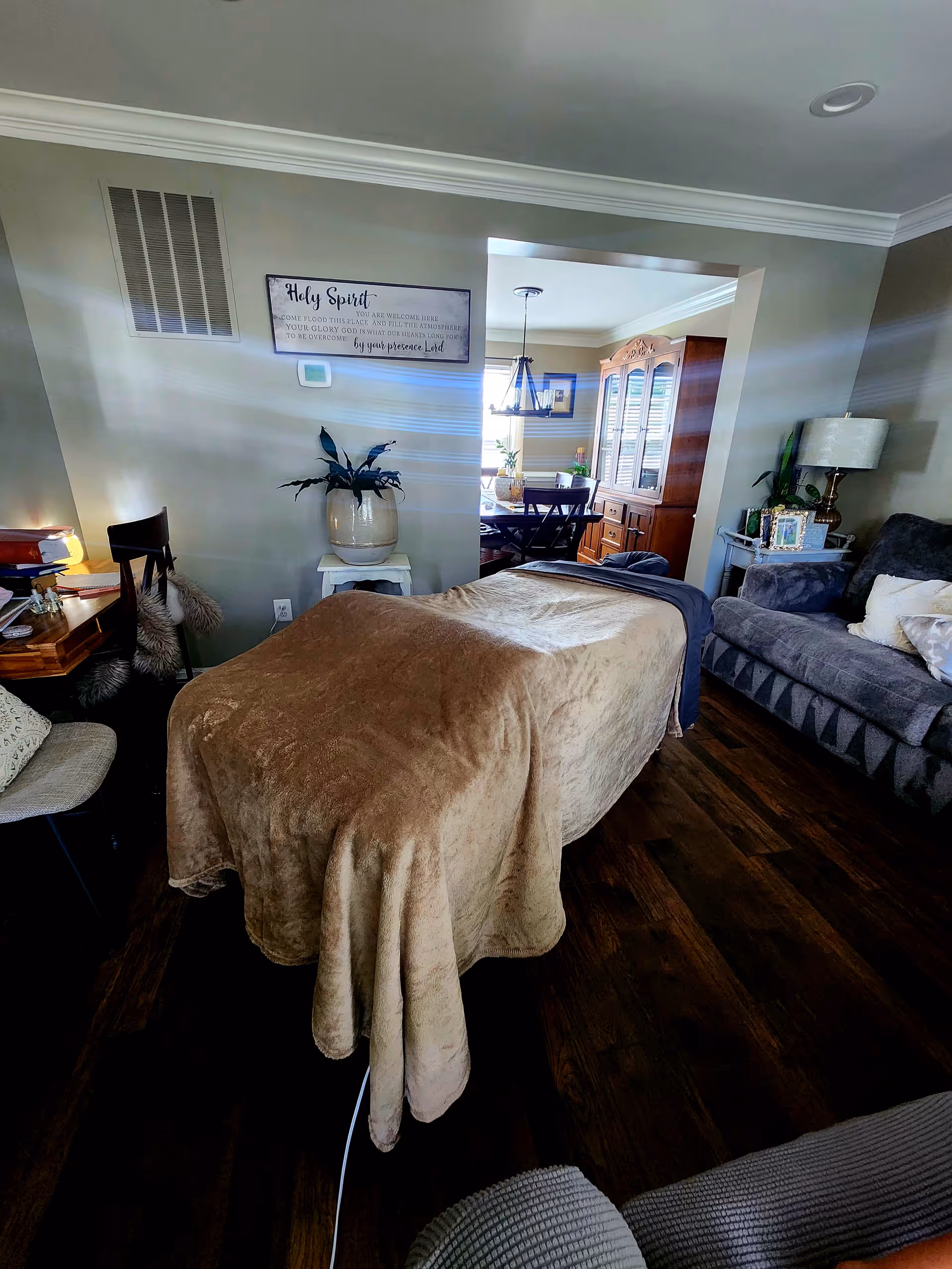 A massage table covered with a beige blanket sits in a cozy living room.