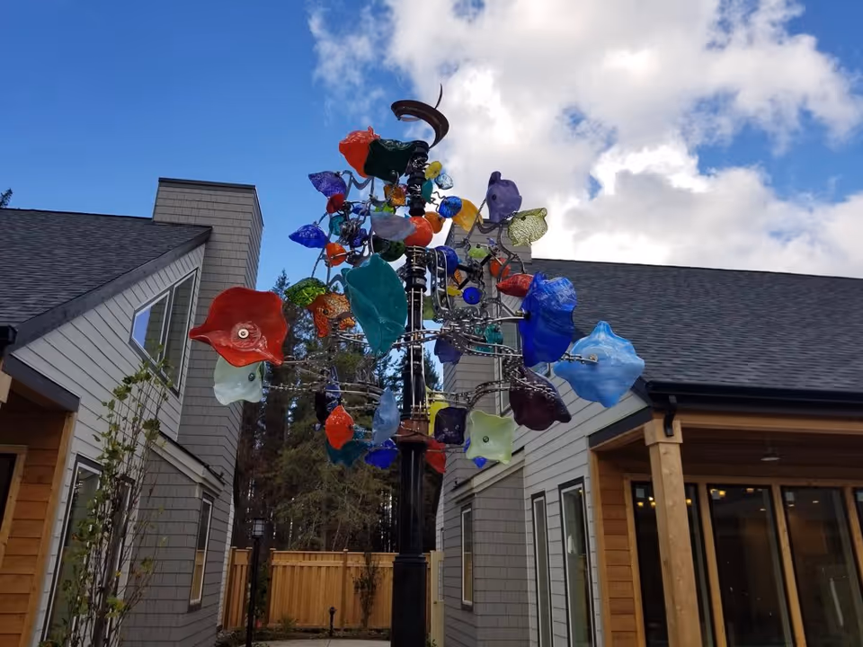 Colorful glass sculpture tree in a cottage-style senior living courtyard, flanked by modern buildings.