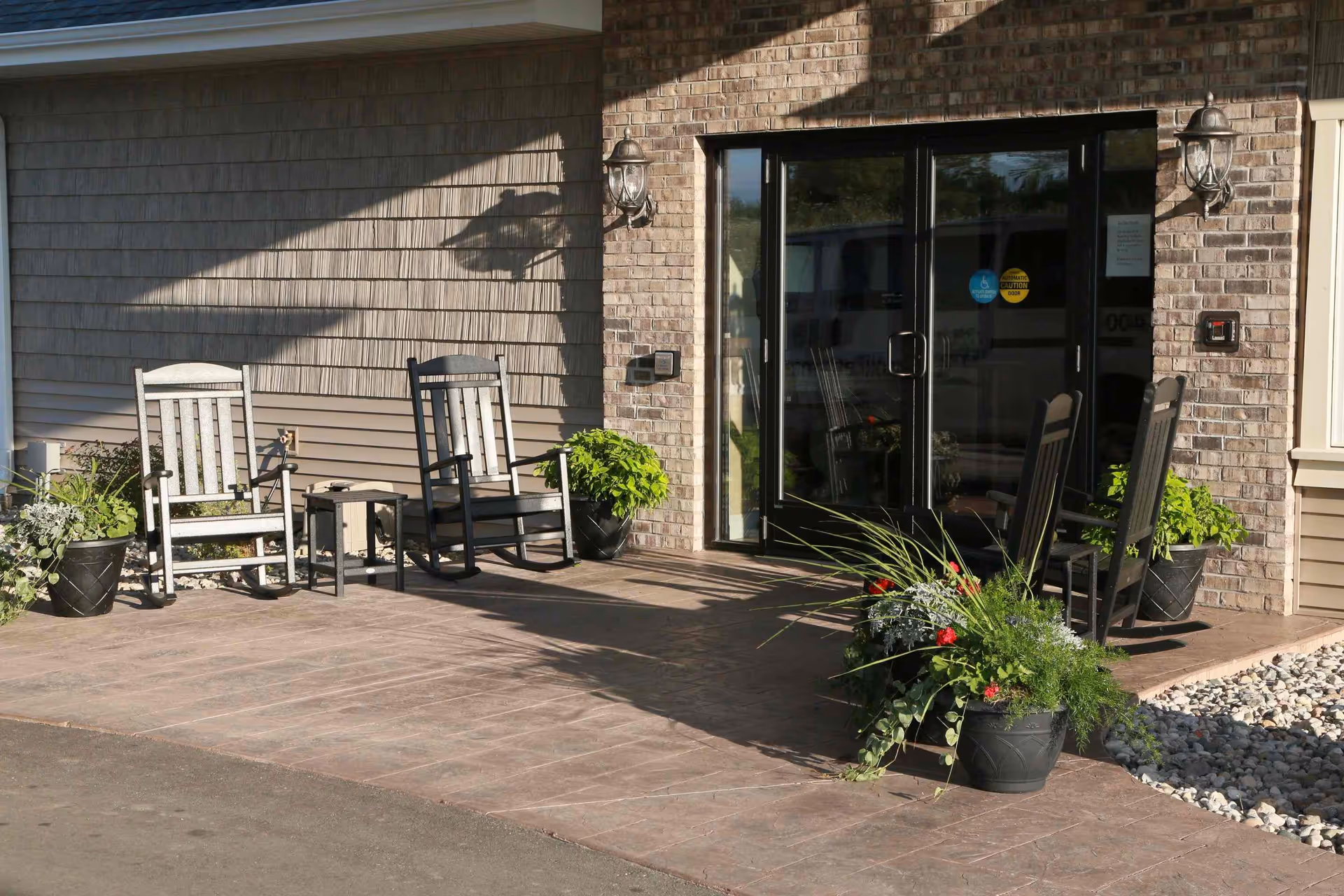 Front entrance patio with glass double doors, several rocking chairs, and potted plants.