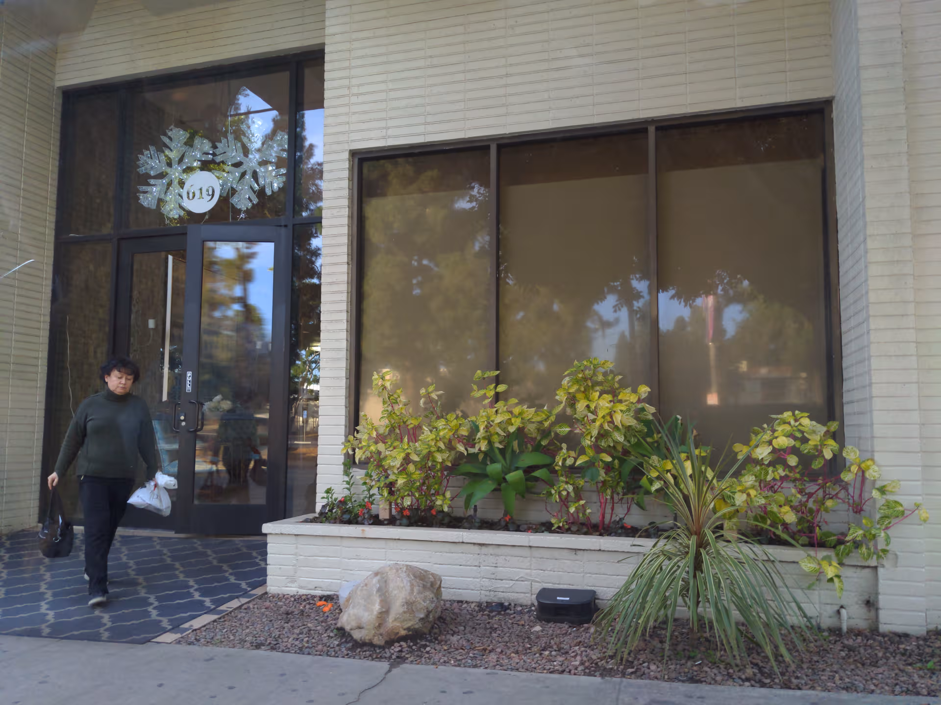 Person exits Kennedy Care Center front entrance featuring glass doors, large windows, and planter bed.