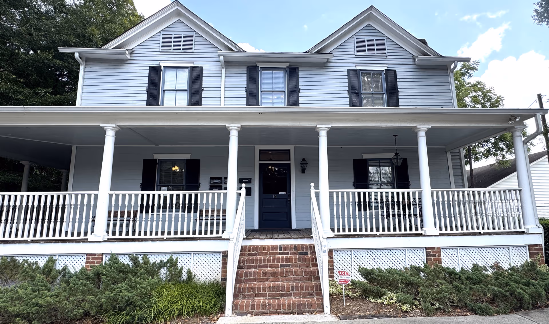 Front view of a two-story house-style building with a wide porch and brick steps.