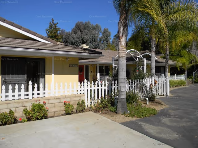 Single-story senior care home, Sagadraca Care Home, with yellow walls, white picket fence, palms.