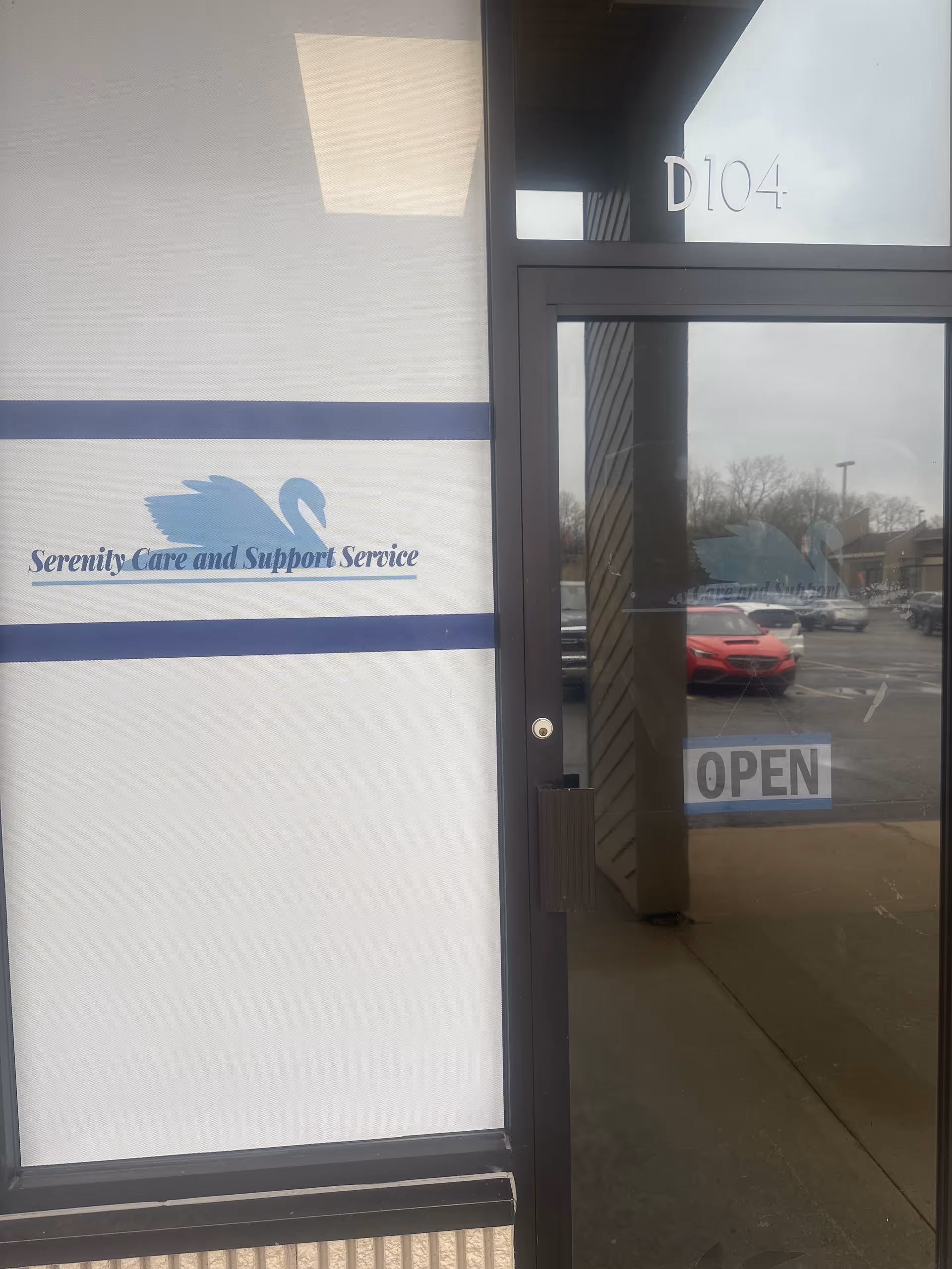 Entrance to Serenity Care and Support Service with open sign, glass door, parking lot outside.