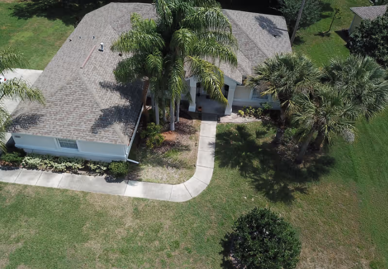 Aerial view of a single-story senior living facility with palm trees and curved entrance path.