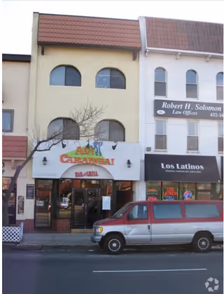 Street view of a storefront row with a restaurant, bar & grill signage, and a van.