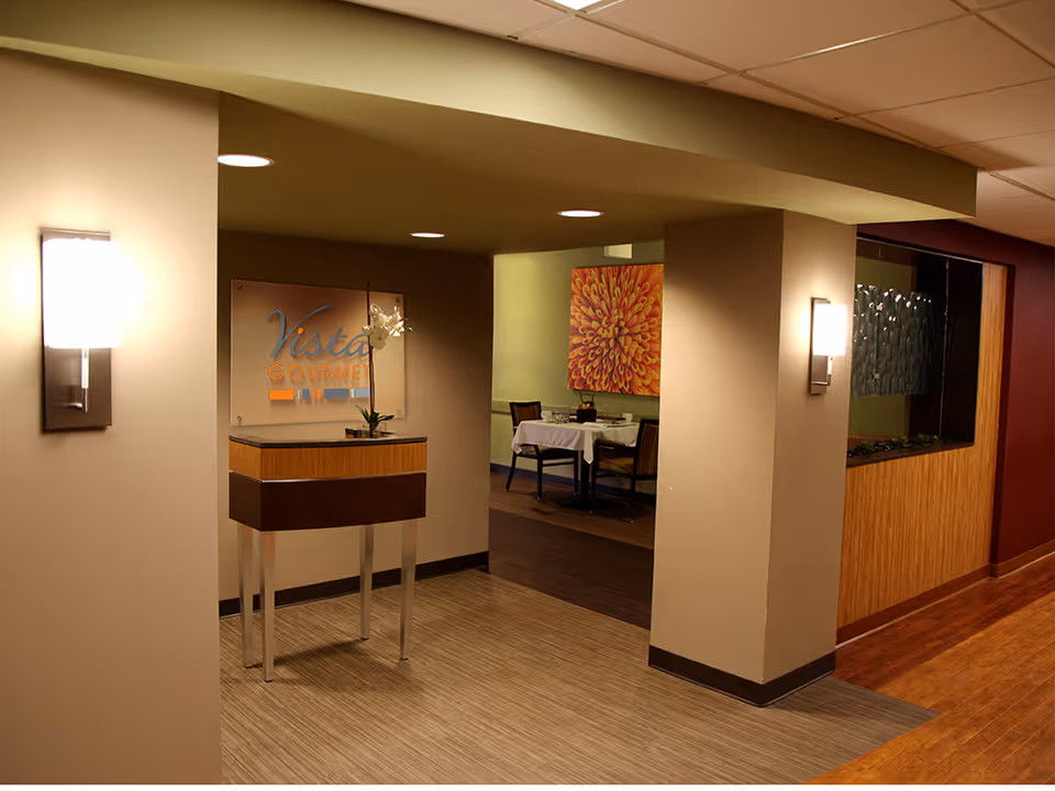 Dimly lit interior corridor with a reception desk and a dining area in the background.