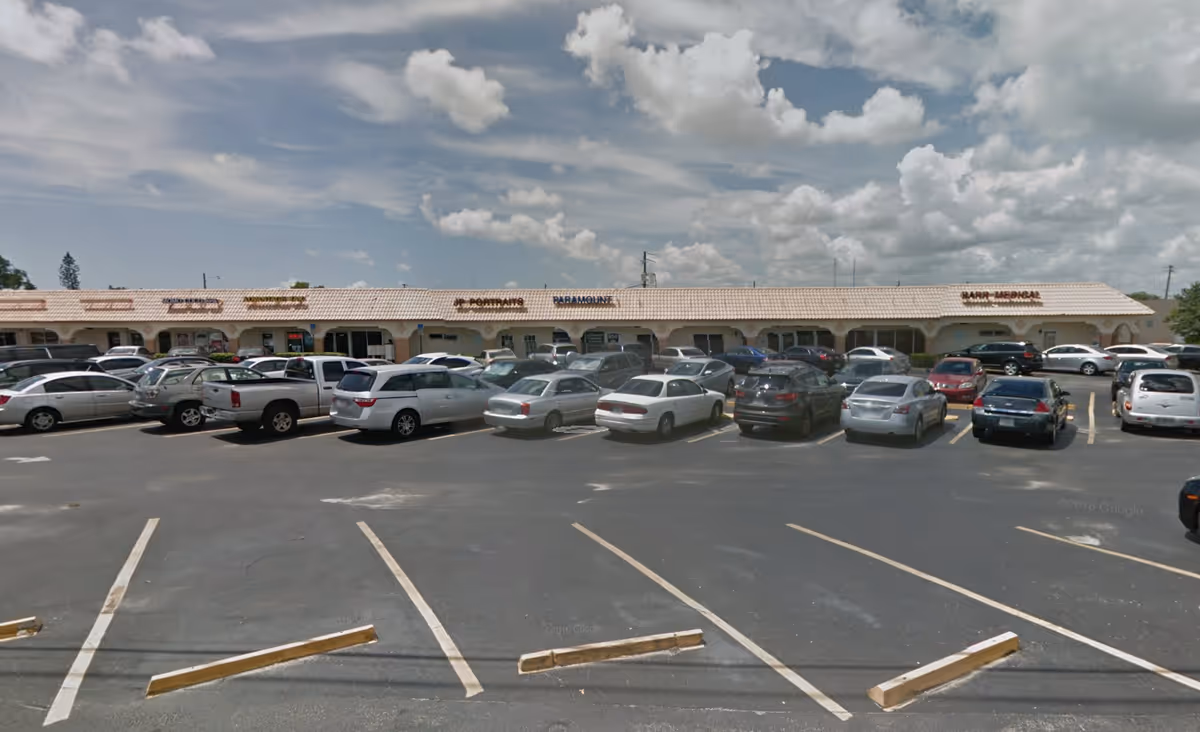 Exterior view of a strip mall with storefronts and parked cars.