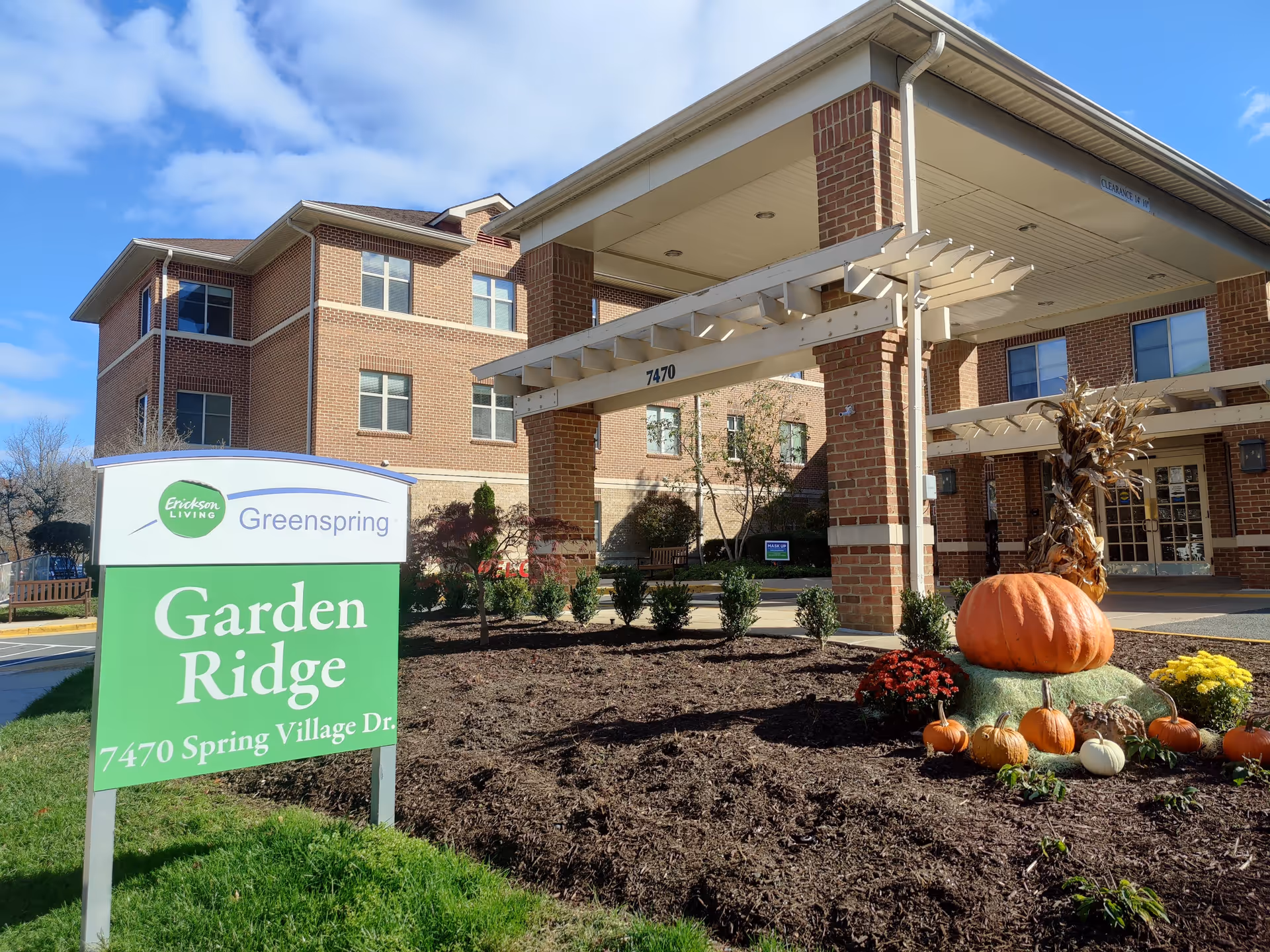 Exterior view of a brick senior living building with entrance and pumpkins.
