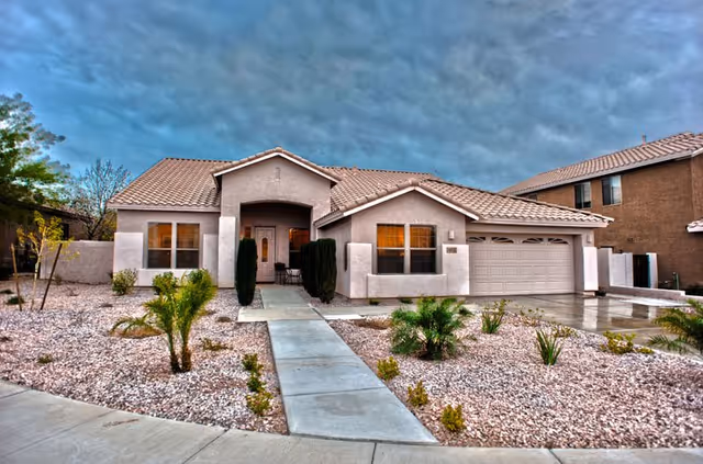 Front view of a beige stucco house-style building with a two-car garage and desert landscaping.