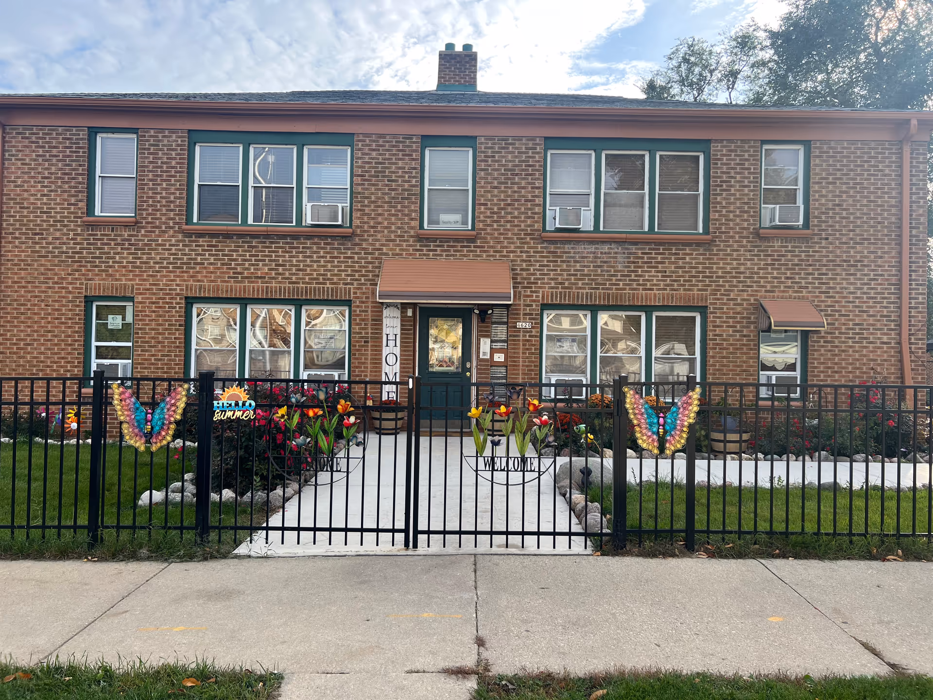 Brick two-story senior housing building with a gated front yard and colorful flowers.