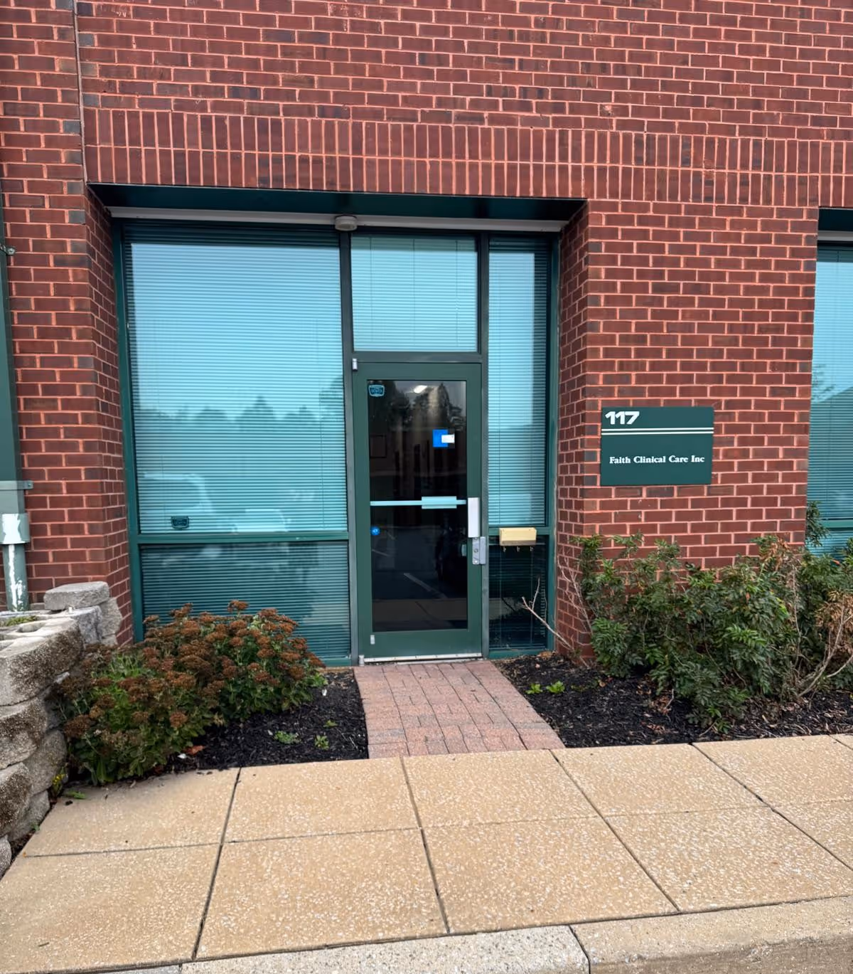 Brick building facade with glass entrance door and Faith Clinical Care Inc sign at 117