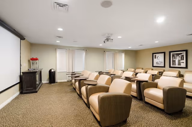 Small screening room with rows of beige reclining theater chairs facing a large projection screen.