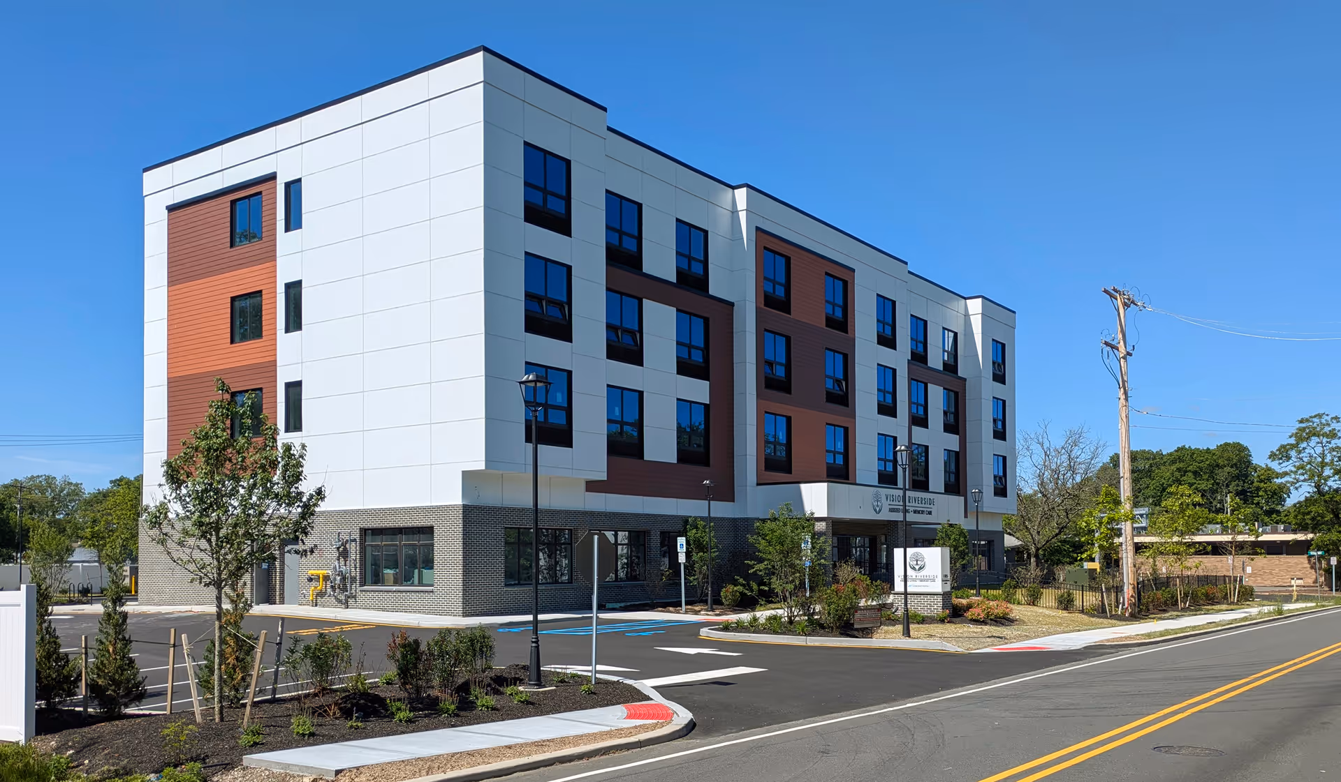 Modern four-story building with white and brown panels, signage, and a parking lot under blue sky.