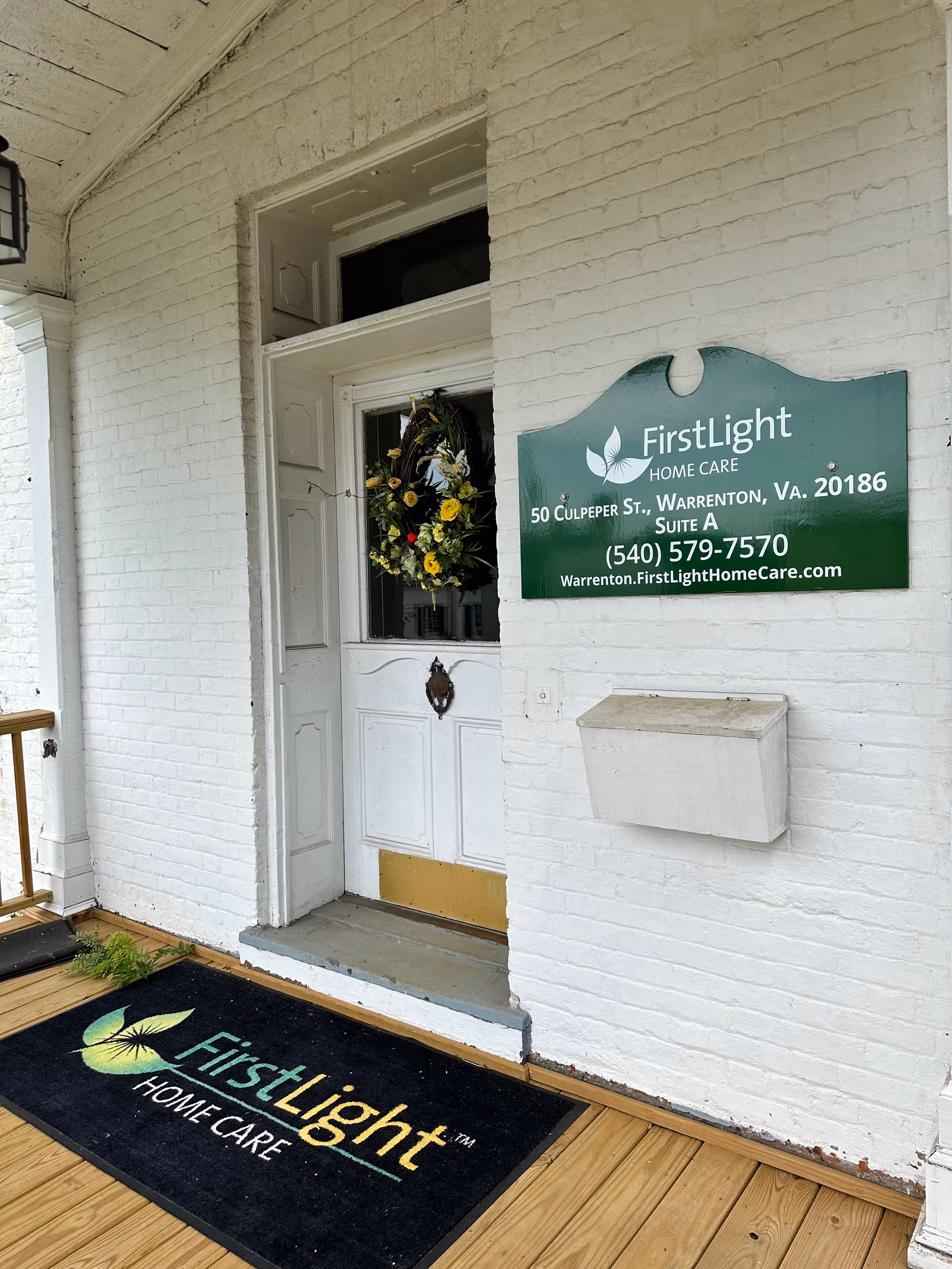 White brick building entrance with wreath on door, FirstLight Home Care sign and logo on wall.