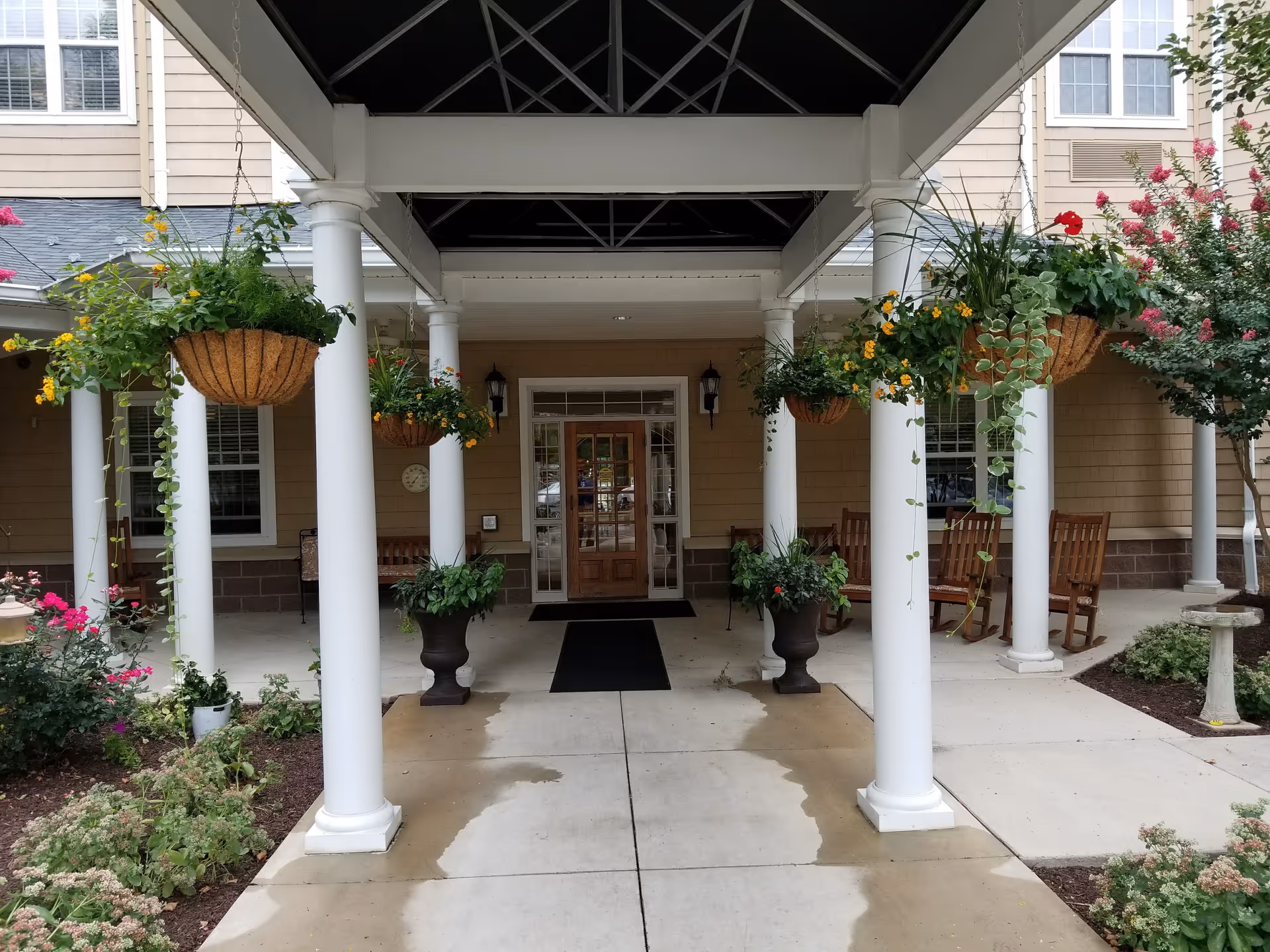 Covered entrance with white columns, hanging baskets, benches, and potted plants at AVIVA Baldwin Park.