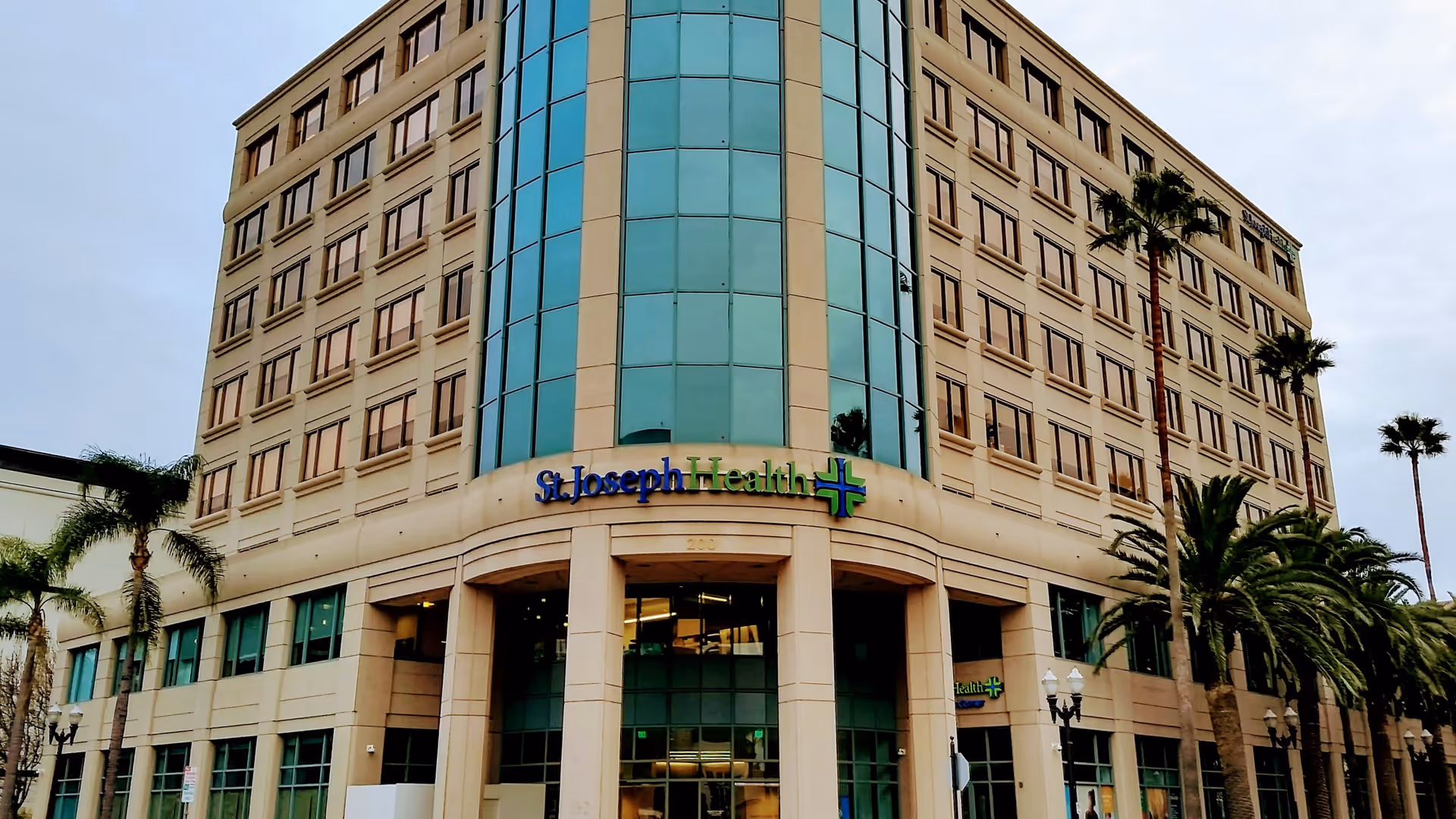 Facade of a tall beige medical building with St. Joseph Health signage and palm trees.