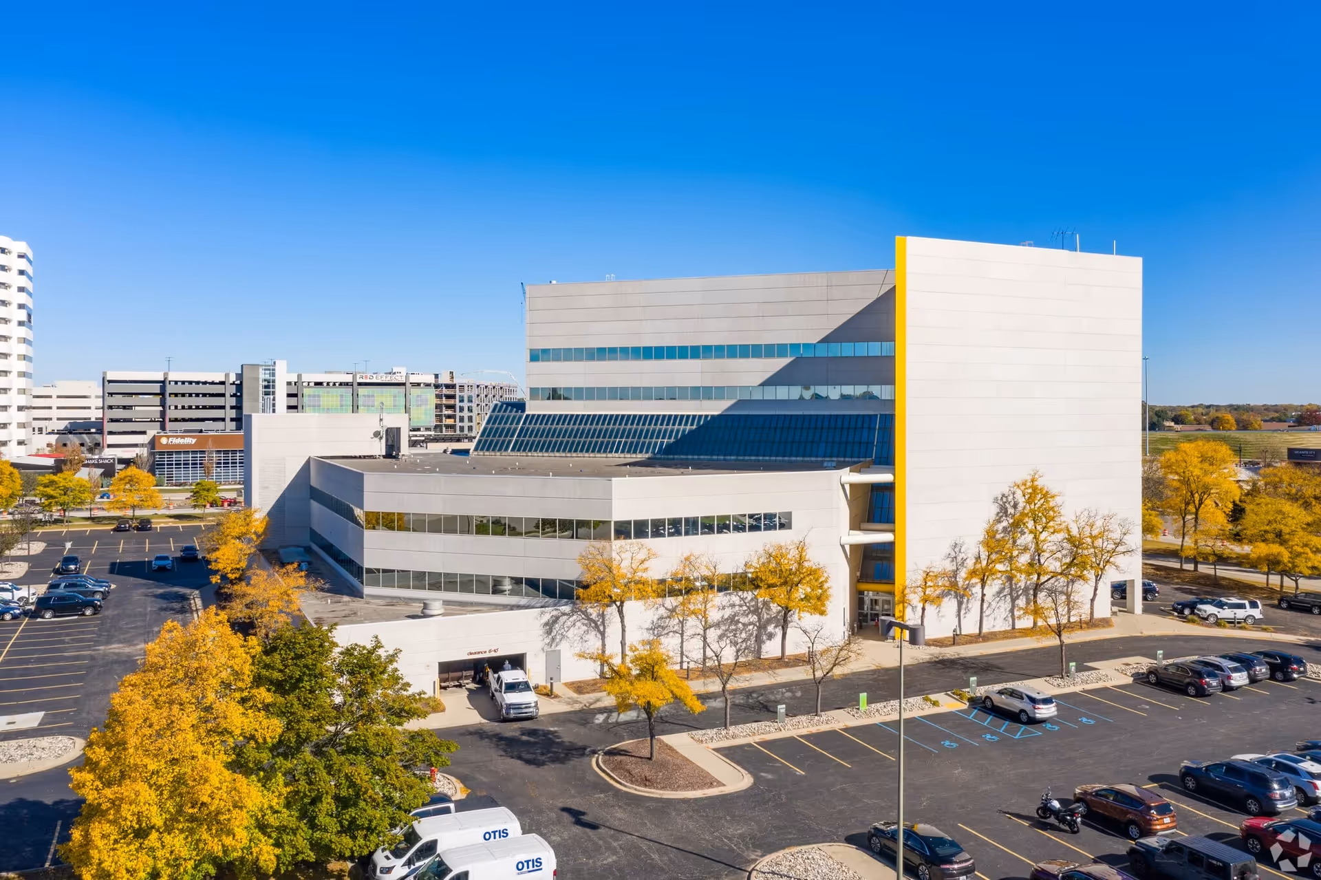 A large modern facility exterior with white walls, glass, and a surrounding parking lot.