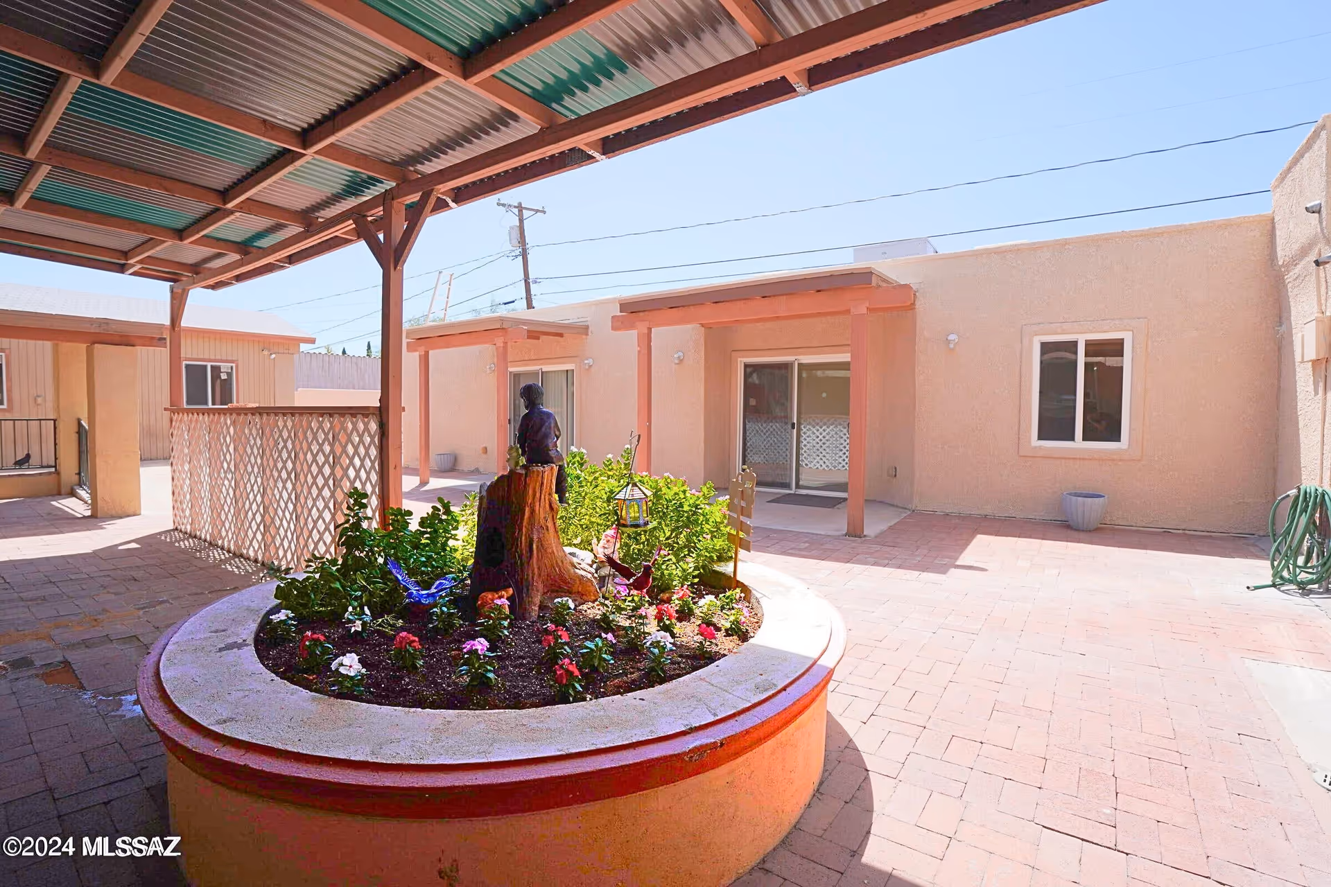 Outdoor courtyard with a circular flower bed under a covered walkway beside beige building.