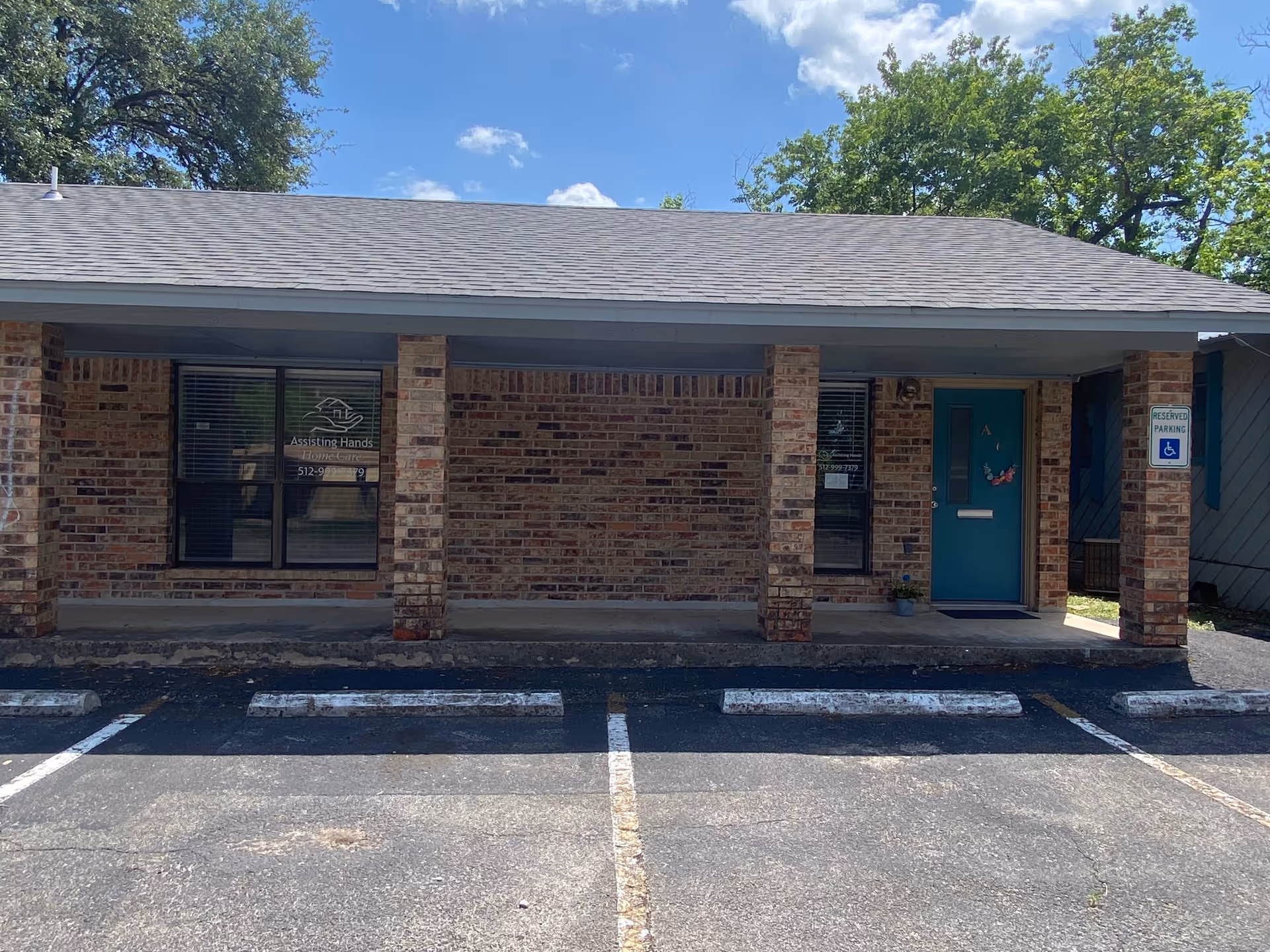 Brick storefront for Assisting Hands of West Austin with blue door and parking lot.