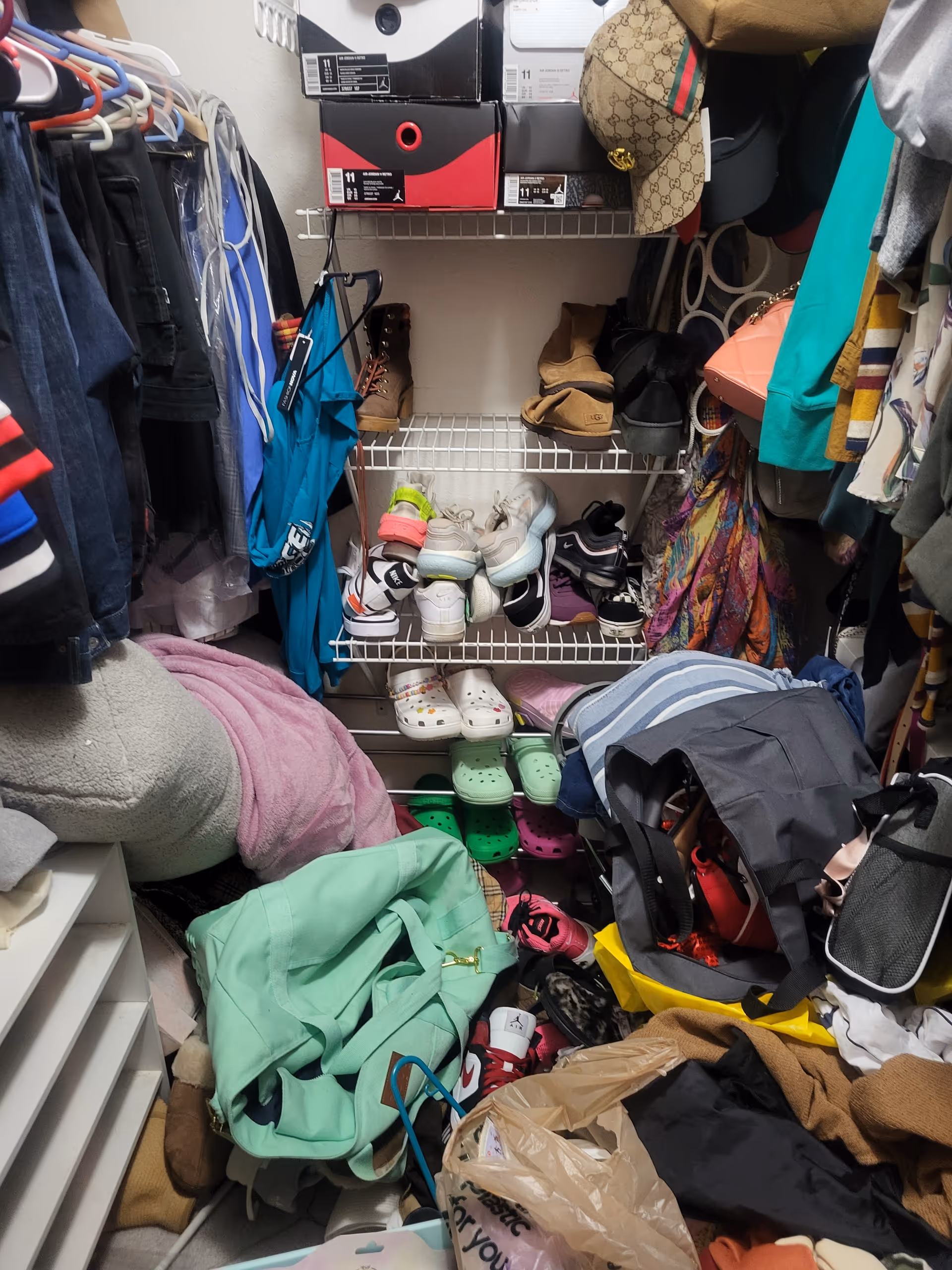 Cluttered closet with shelves, shoes, jackets, bags, and boxes stacked.