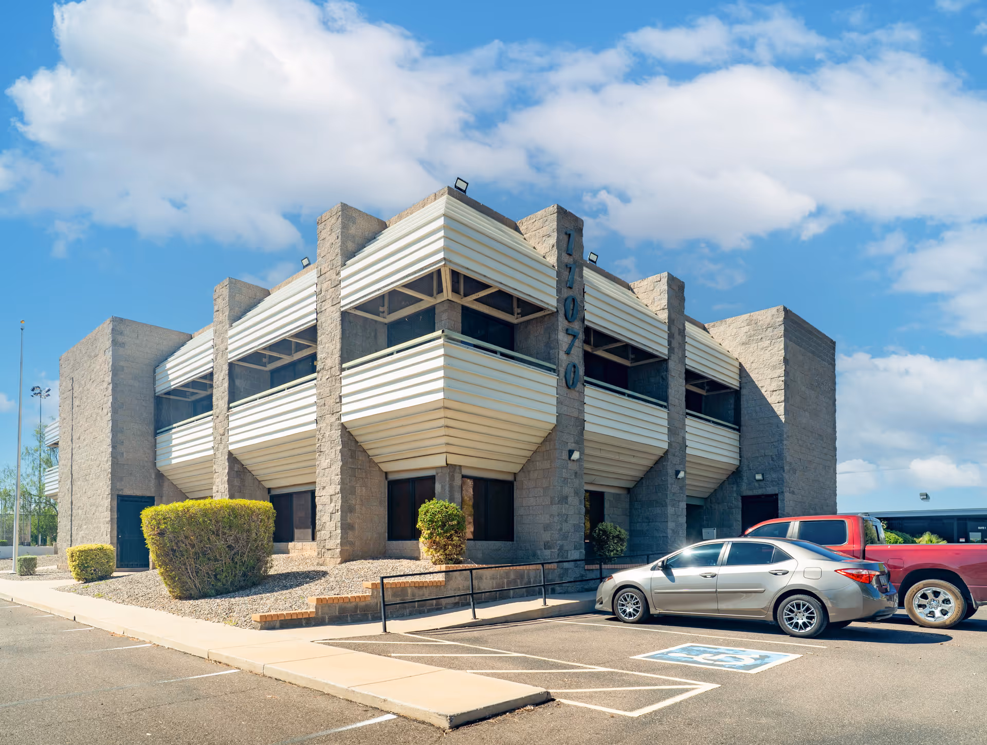 Exterior view of a modern stone-clad building with white horizontal accents and parked cars.