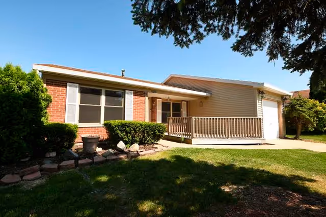 Single-story senior living facility front with brick, siding, a porch, and a green lawn.