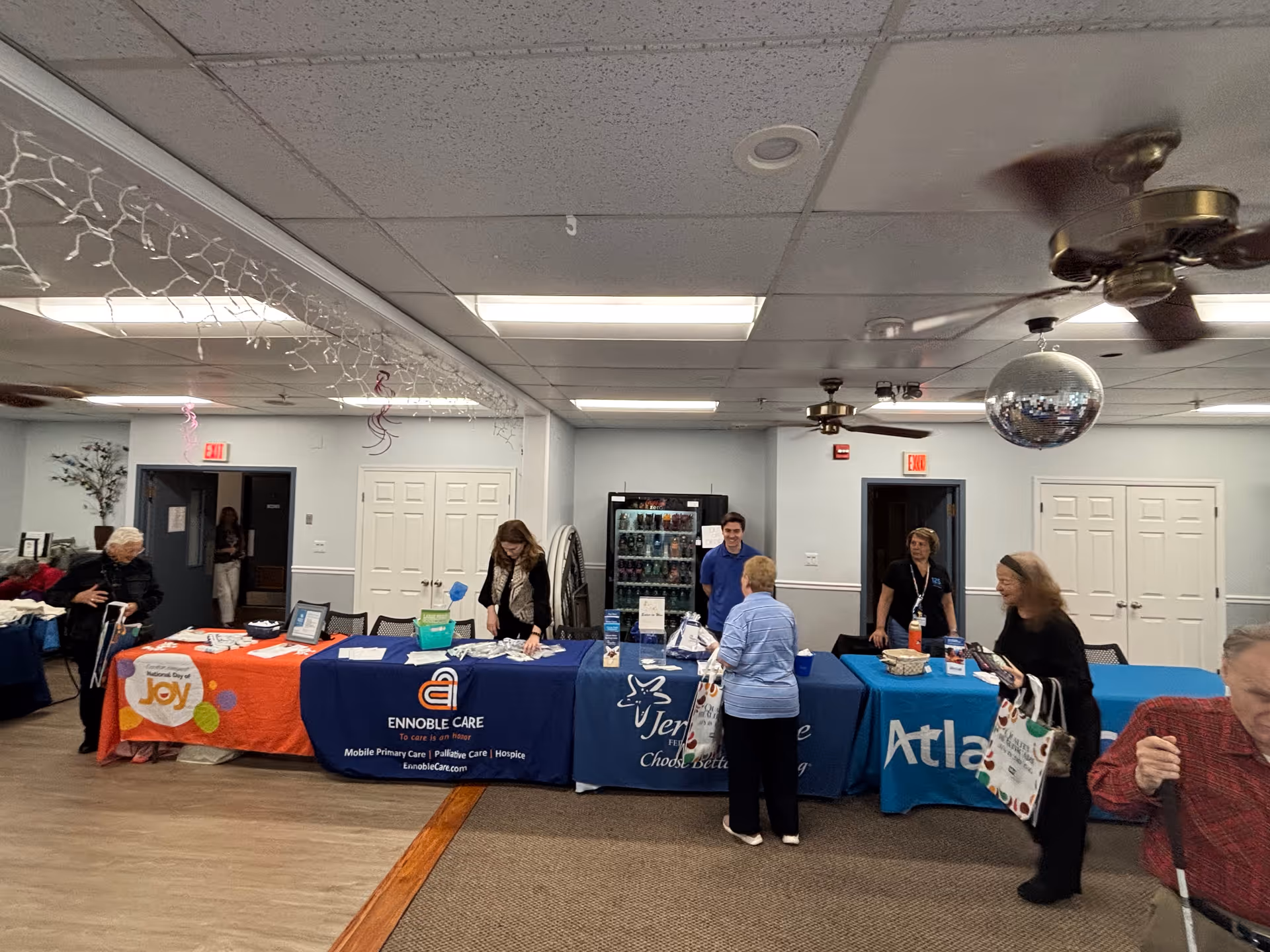 Indoor community fair in a senior care facility with vendor tables and attendees.