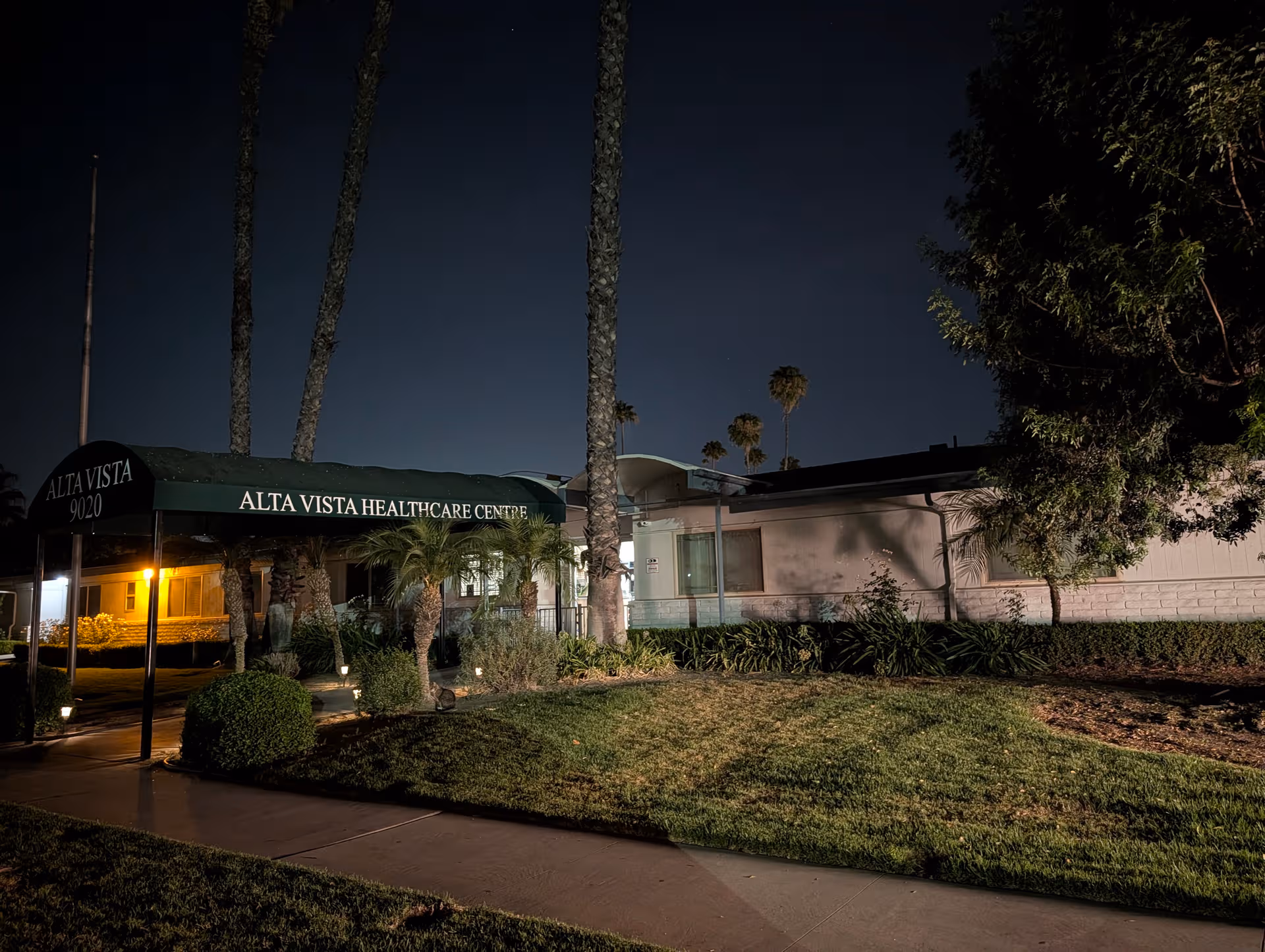 Night exterior of Alta Vista Healthcare Centre with a sign canopy at the entrance.