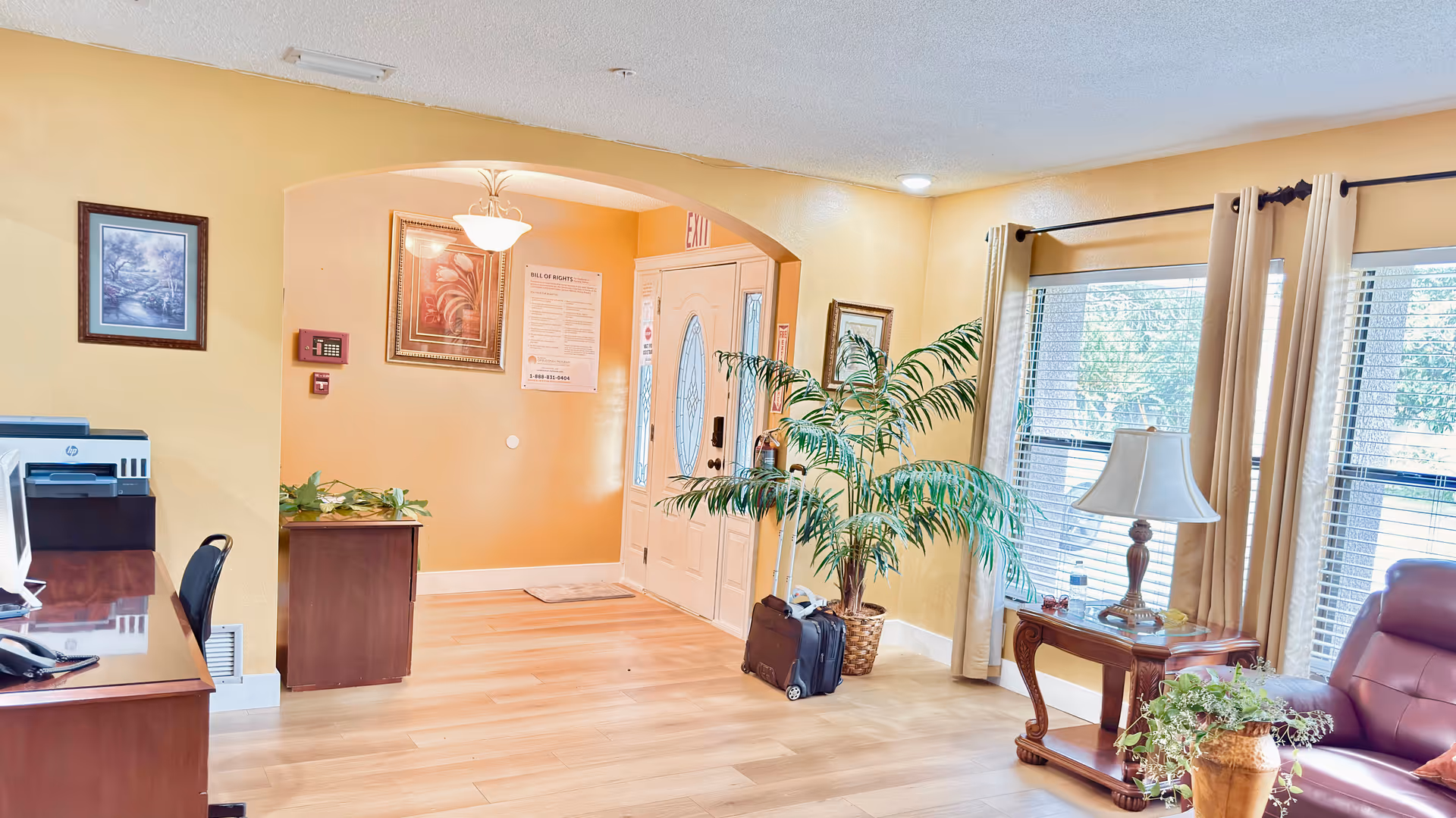 Bright Ajr Loving Care ALF lobby with front door, desk, sofa, lamp, and plants.