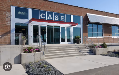 Brick building entrance with glass doors, concrete stairs, railings, and potted plants.