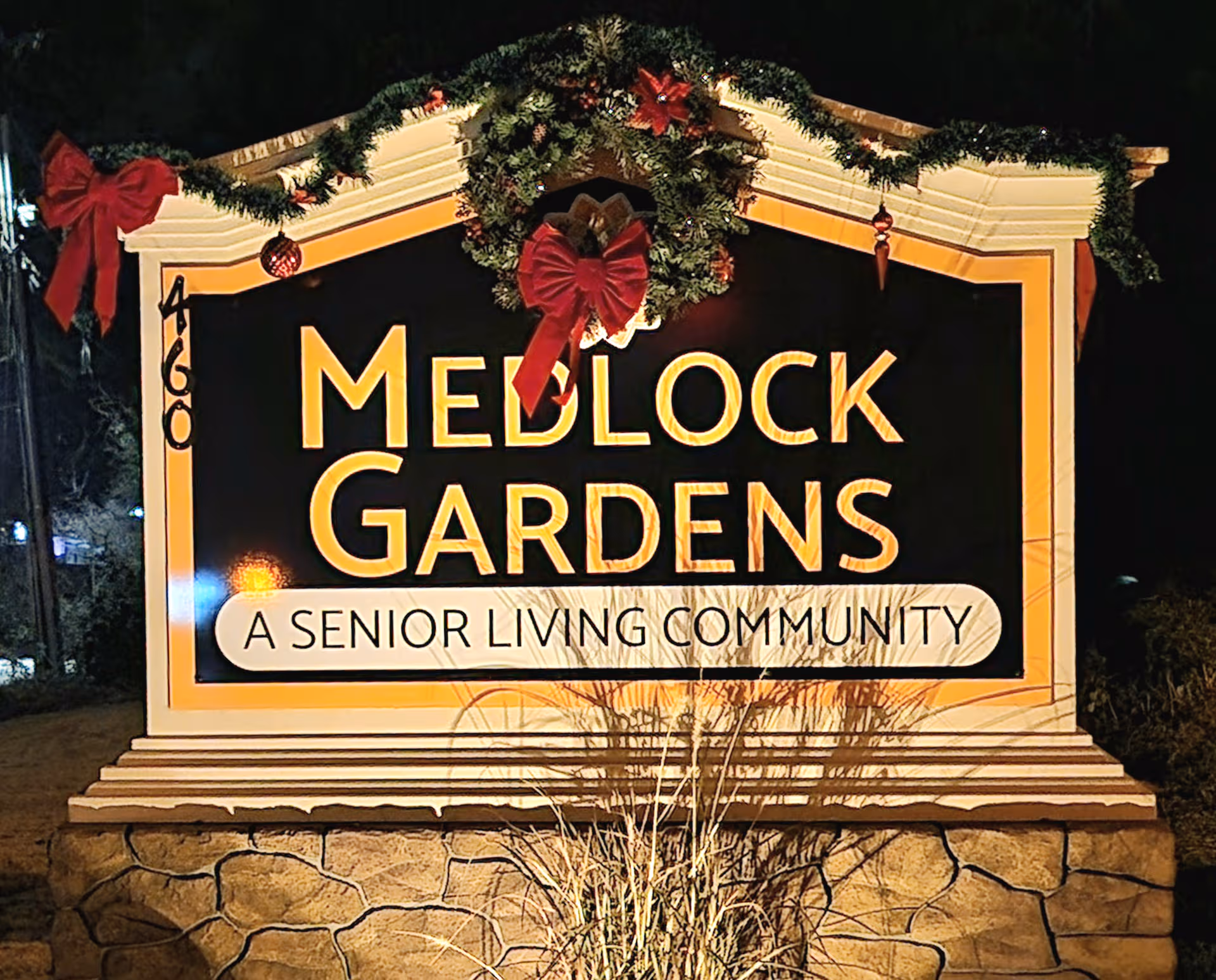 Outdoor sign reads Medlock Gardens Senior Living Community, adorned with festive wreaths.