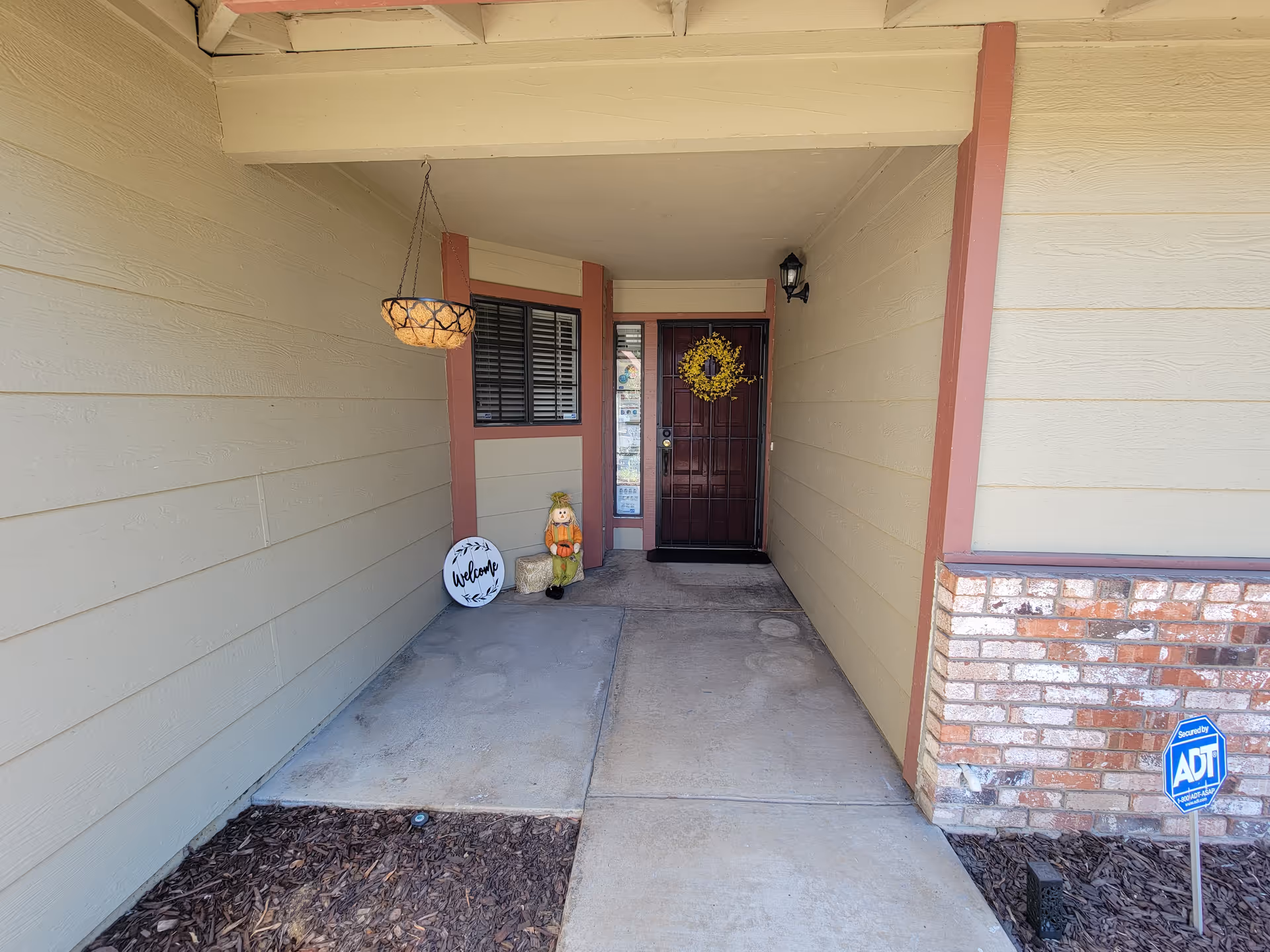 Front entrance of a residential building with wreath, welcome sign, and Halloween decor.