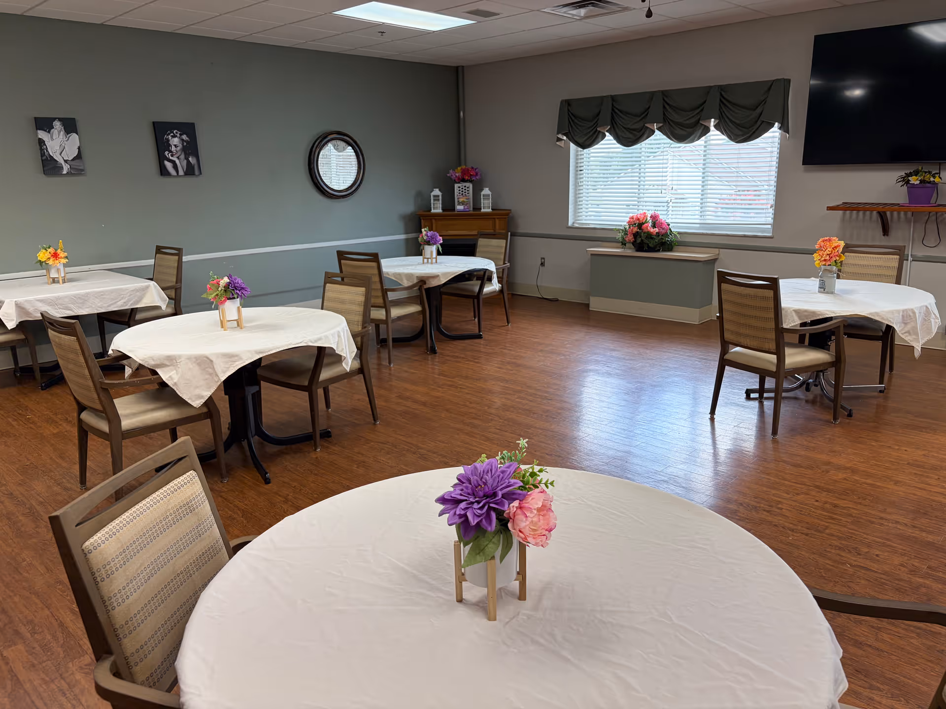 A dining room in a senior living facility with round tables and floral centerpieces.