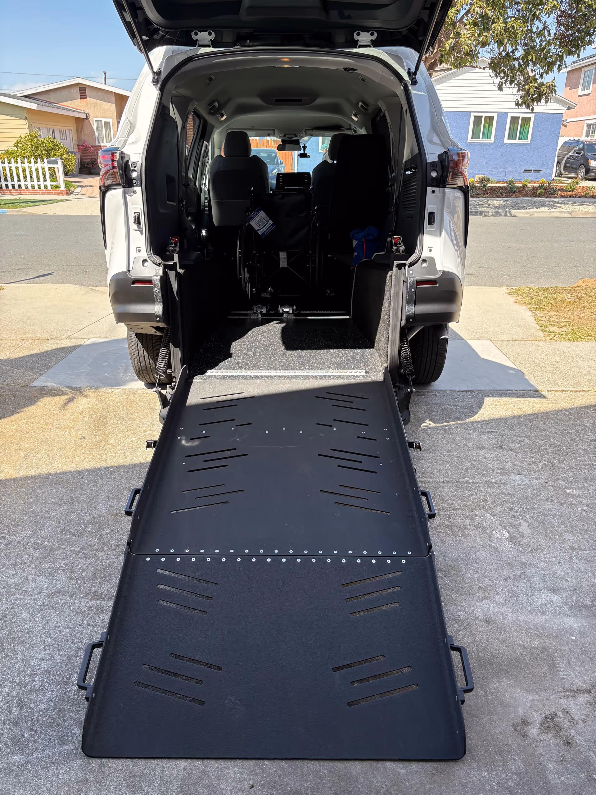 Rear view of a wheelchair-accessible van with an extended ramp on a driveway.
