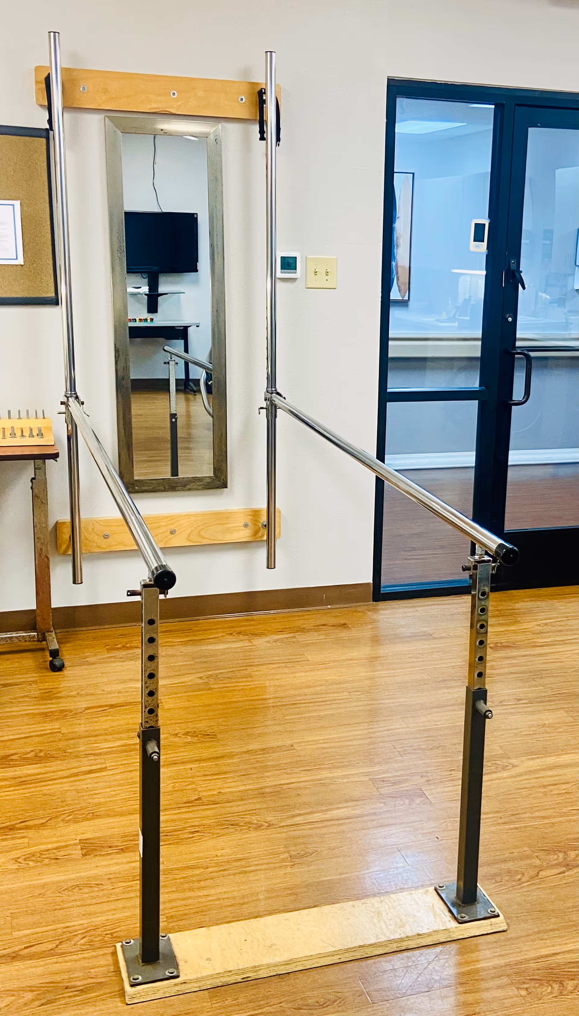 Interior rehab space with parallel bars, a mirror, and doorway in a senior living facility.
