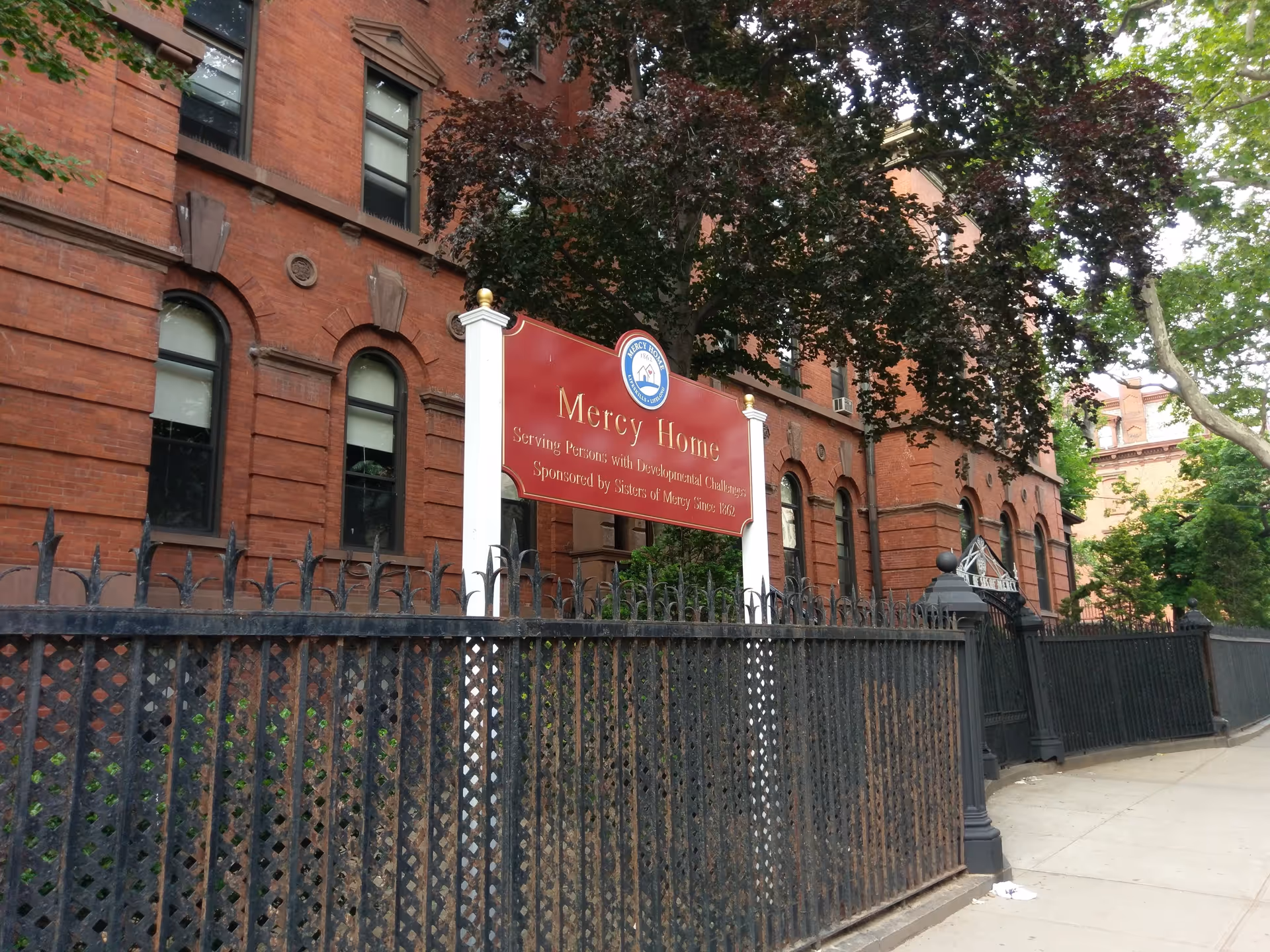 Red brick Mercy Home for Children building with a black iron fence and sign.
