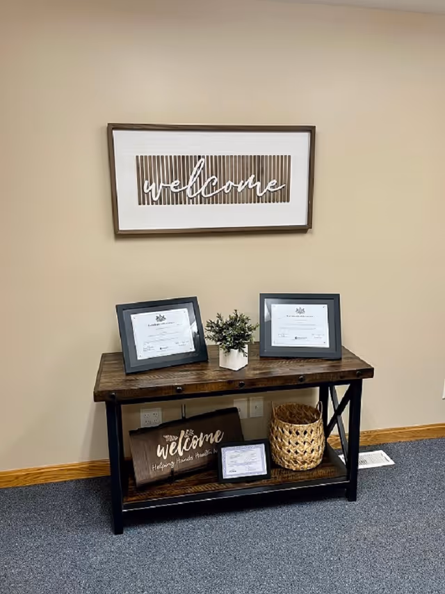Interior entry area with a wooden console table, welcome sign, frames, and a plant.