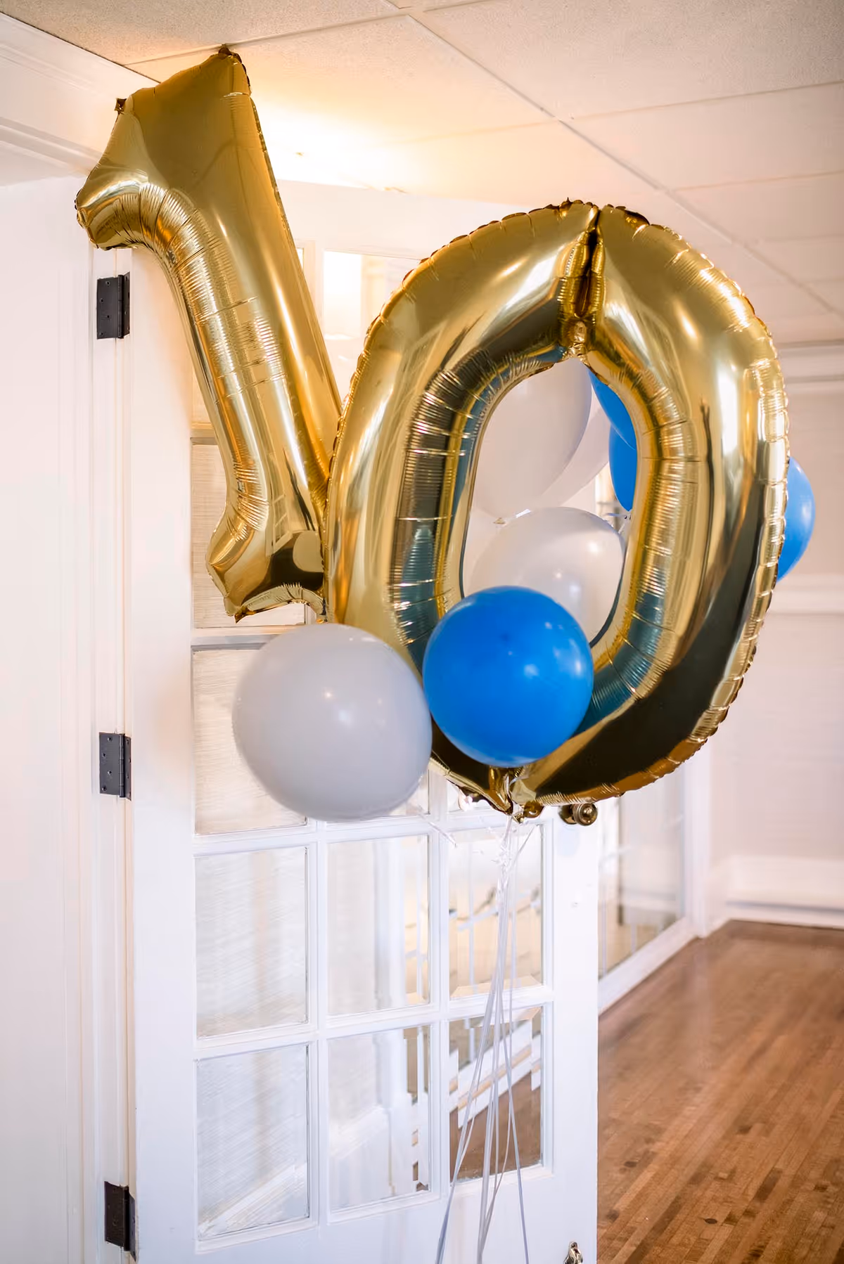Gold number balloons 10 with blue and white balloons by a glass-paneled interior door.
