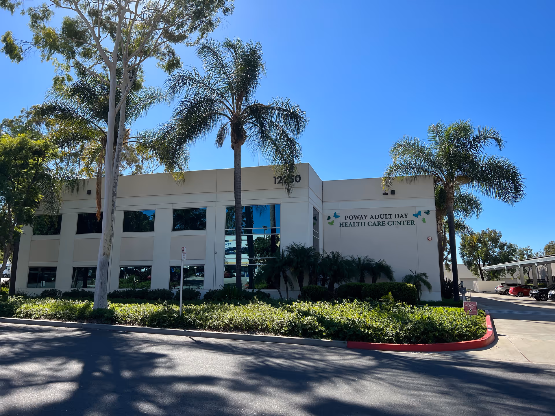 Exterior view of Poway Adult Day Health Care Center with palm trees and landscaping.