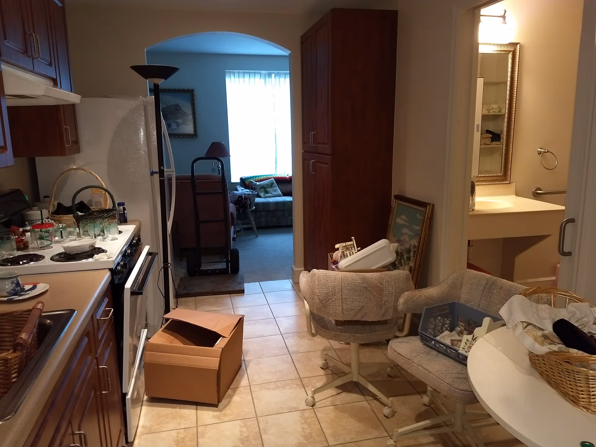 Cluttered senior living kitchen and seating area with a box near the hallway.