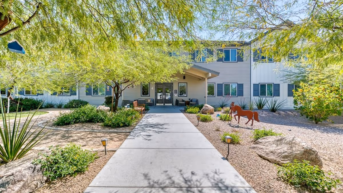 Front exterior view of Paradise Valley Senior Living with a walkway, desert landscaping, and trees.