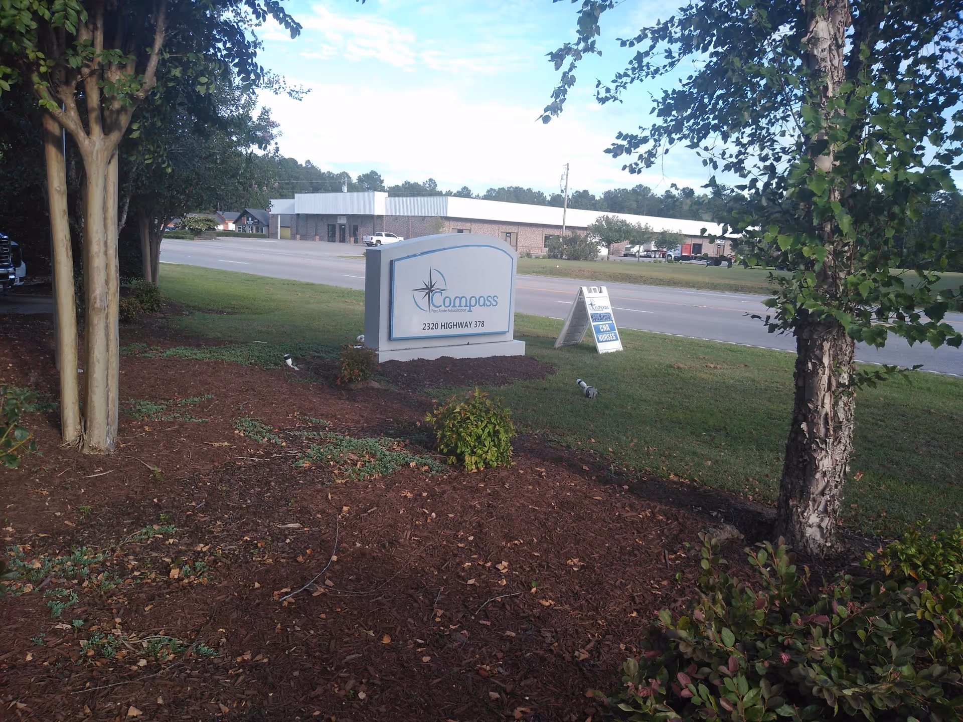 Exterior view of Compass Post Acute Rehabilitation sign with landscaped front and road in background