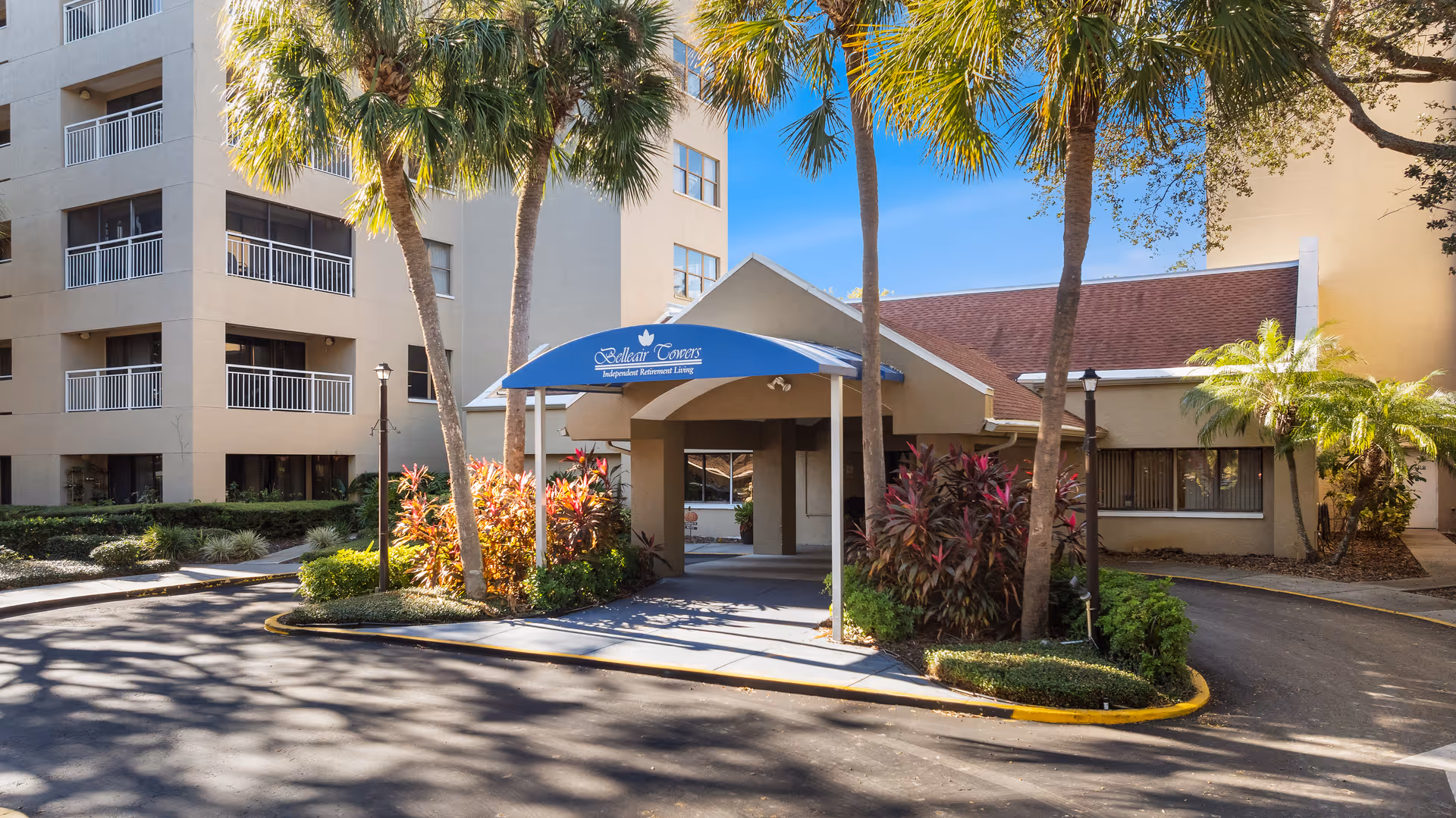 Front entrance of Belleair Towers senior living building with a blue canopy and palm trees.