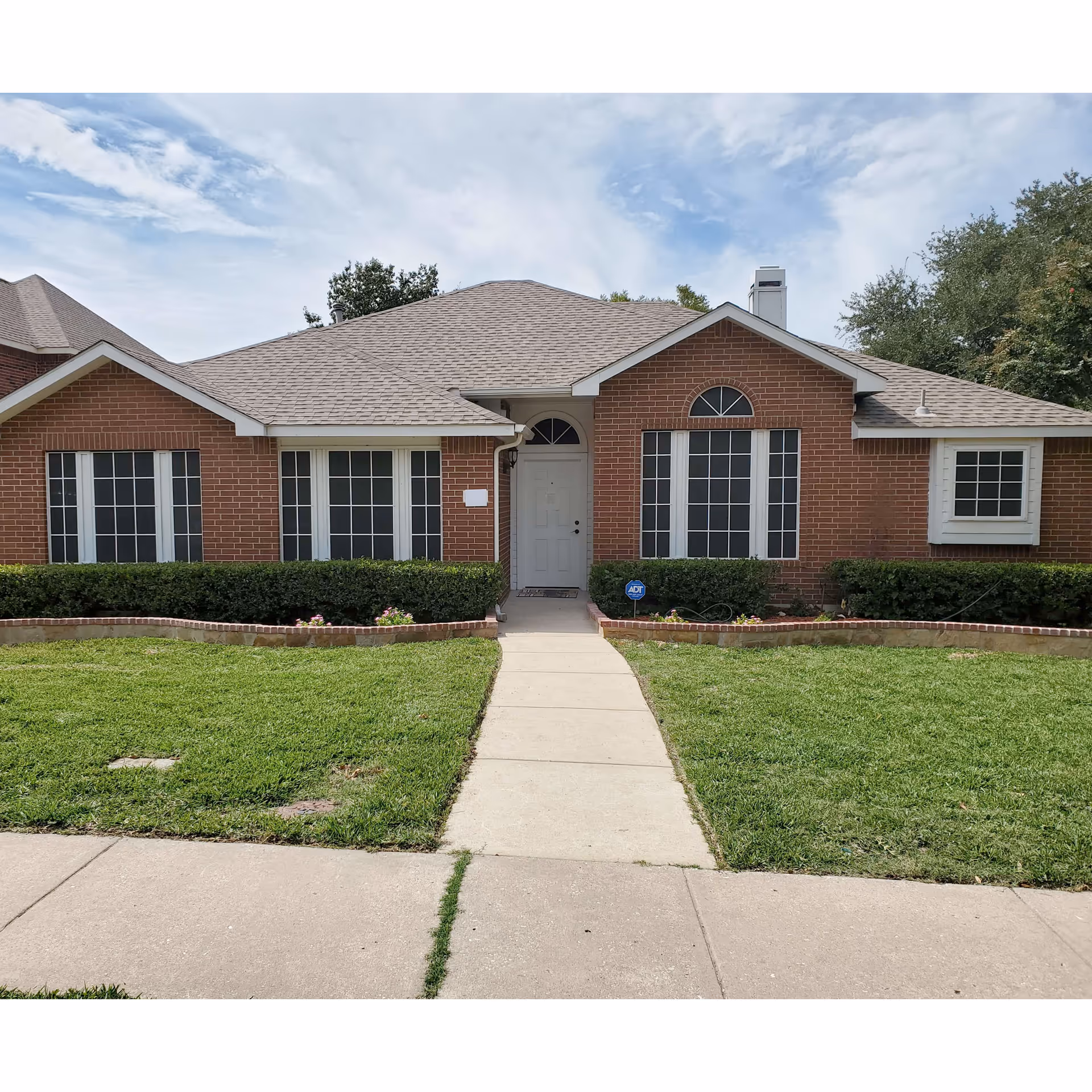 Brick, single-story building with a central door, arched window, and manicured lawn.