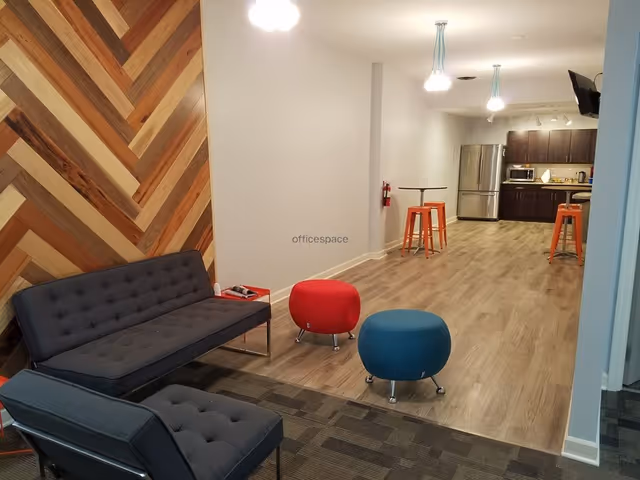 Modern lounge area with gray sofa, colorful ottomans, wooden wall, and open kitchen.
