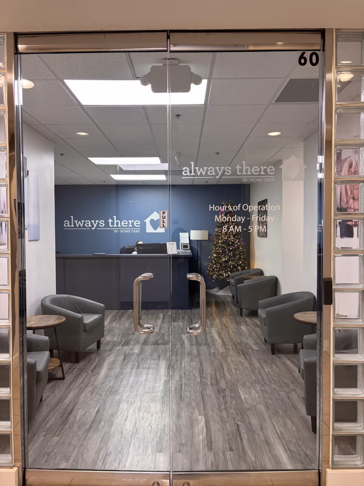 Glass double doors open to a reception area with blue wall, seating, and a Christmas tree.