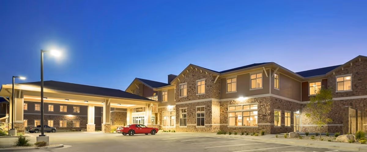 Exterior view of Crescent Senior Living facility at dusk with illuminated windows, a covered entrance, and a red car parked in front.