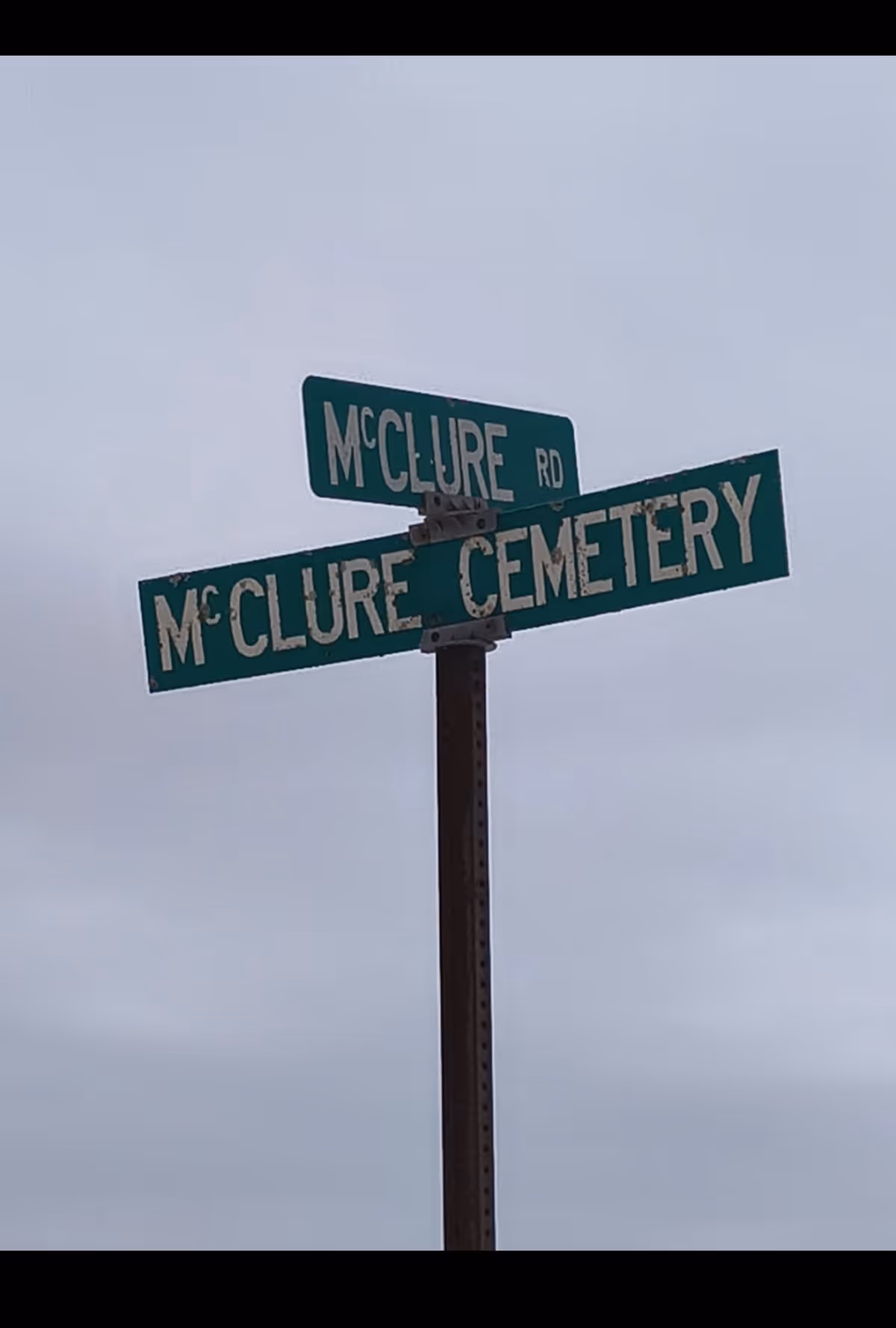 Green street signs read McClure Rd and McClure Cemetery against an overcast sky.